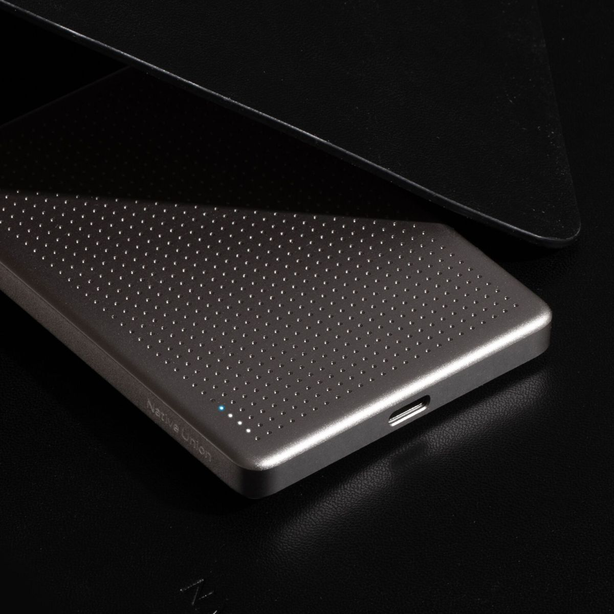 Graue Native Union Powerbank auf schwarzem Untergrund. Ein schwarzes Objekt bedeckt das Gerät teilweise.
