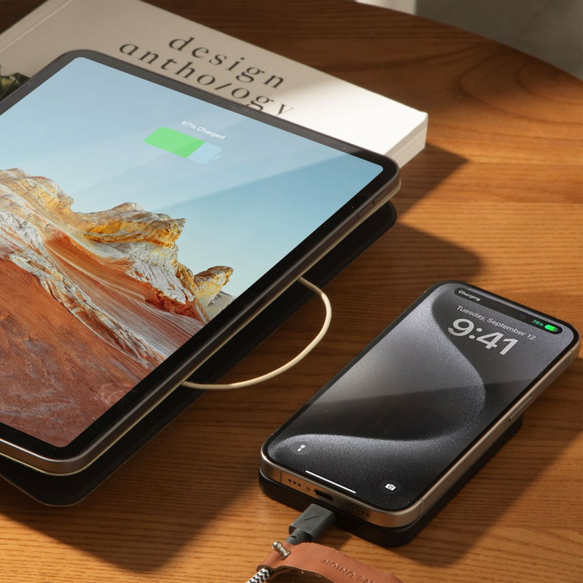 Tablet lädt auf einem Holztisch neben einem Telefon. Ein Buch befindet sich hinter dem Tablet. Telefon zeigt 75% geladen um 9:41 Uhr.