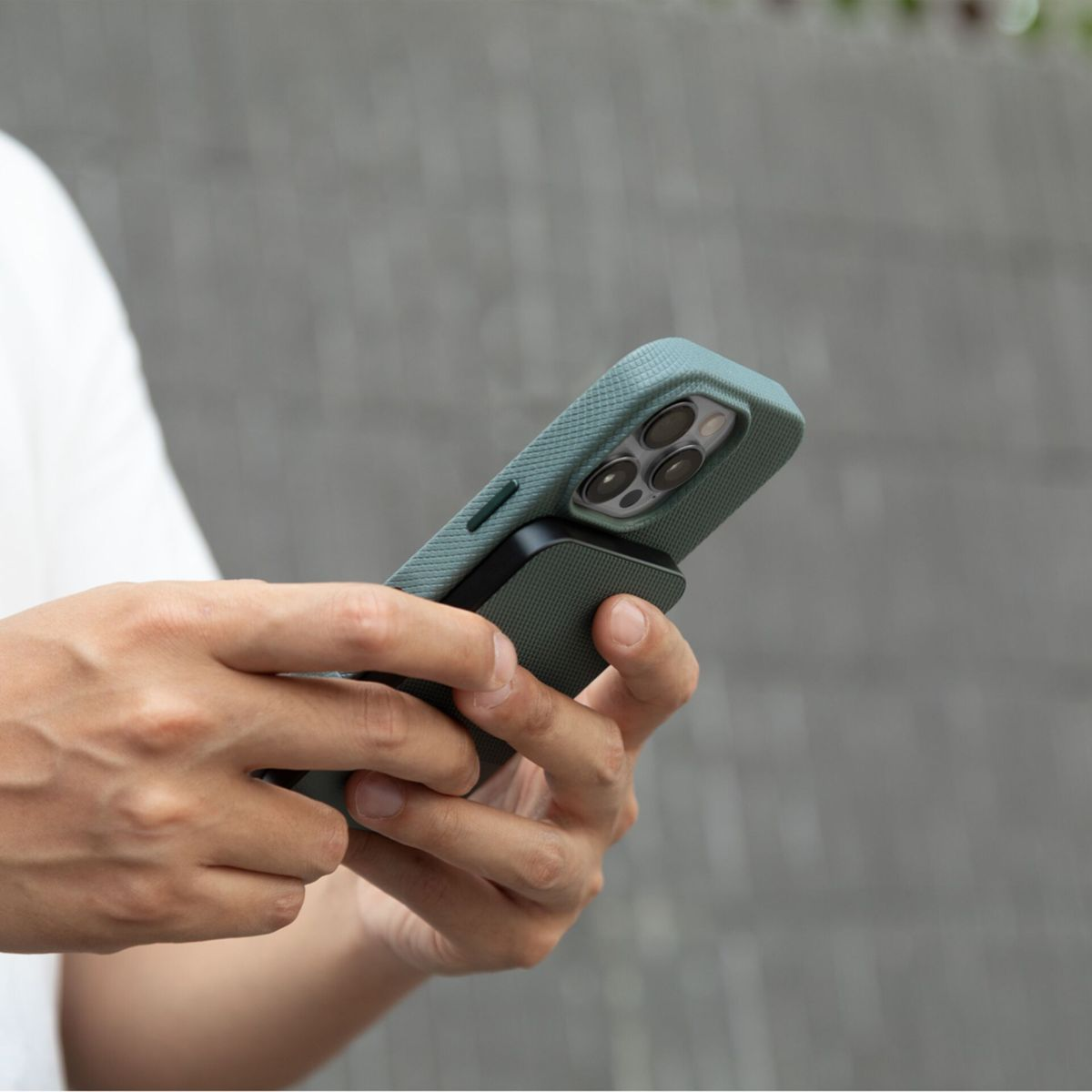 Eine Person hält ein grünes Telefon mit einem schwarzen Zubehör. Der Hintergrund ist eine graue Wand und ein weißes Hemd.