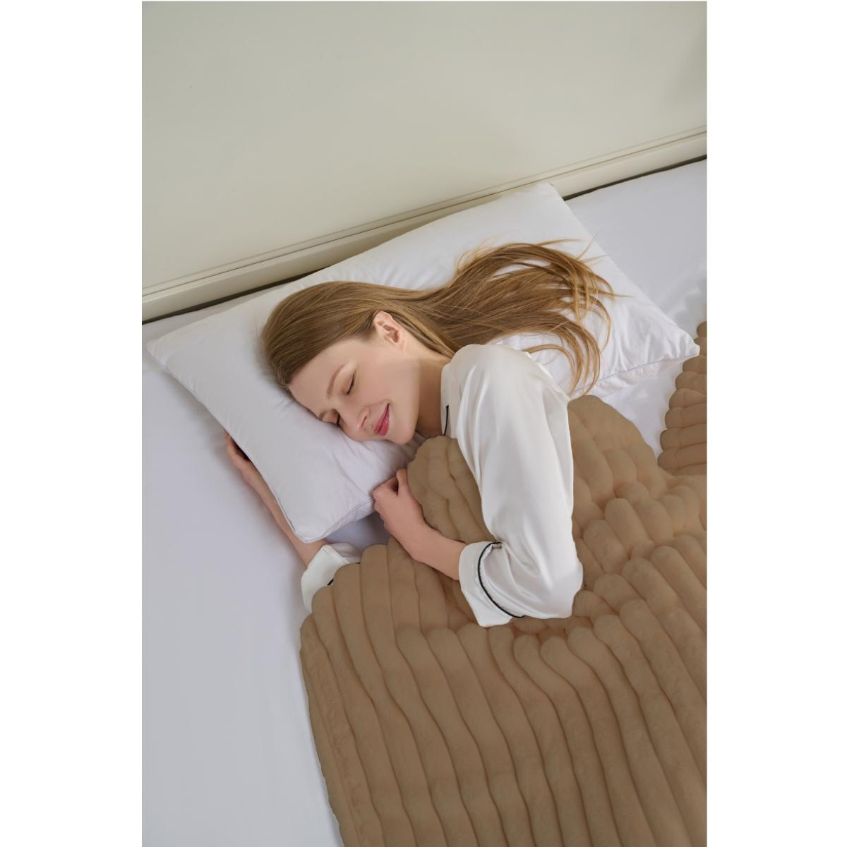 Eine Frau schläft friedlich im Bett, bedeckt von einer braunen Decke. Sie trägt ein weißes Hemd und hat lange blonde Haare.