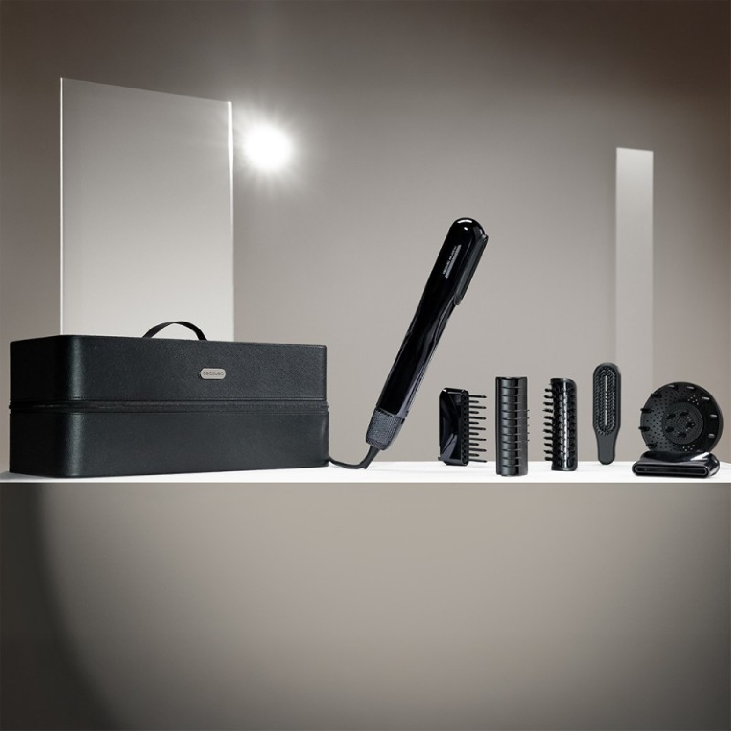 Strumenti per lo styling dei capelli neri su una mensola bianca. Include una borsa, una piastra e vari accessori. Sfondo neutro.