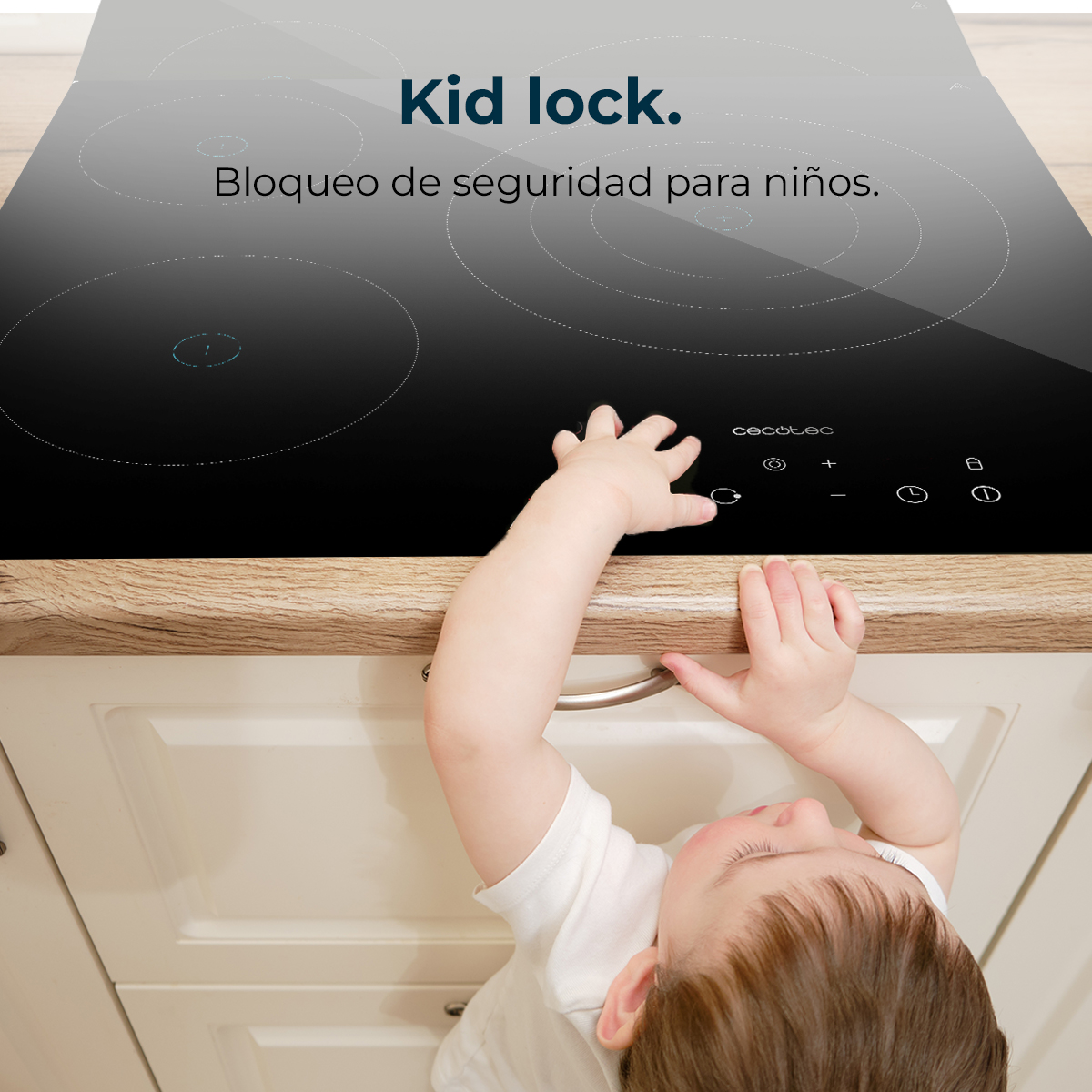 Un bebé alcanza una encimera negra. La estufa tiene zonas de cocción marcadas. Texto dice 'Bloqueo infantil'. El gabinete de la cocina está debajo.