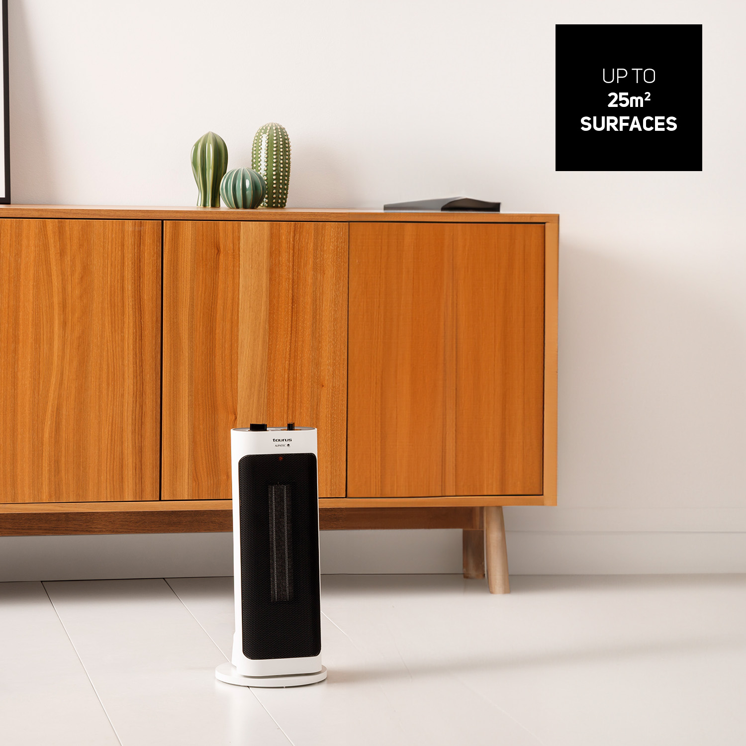 Un riscaldatore bianco e nero è appoggiato su un pavimento bianco. Sullo sfondo un mobile in legno con cactus verdi. Un cartello nero sulla destra.