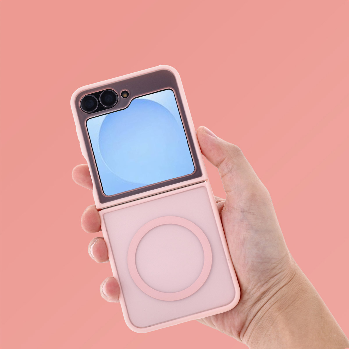 Een hand houdt een roze flip phone hoesje vast. De telefoon is opengeklapt en toont een blauw scherm. De achtergrond is roze.