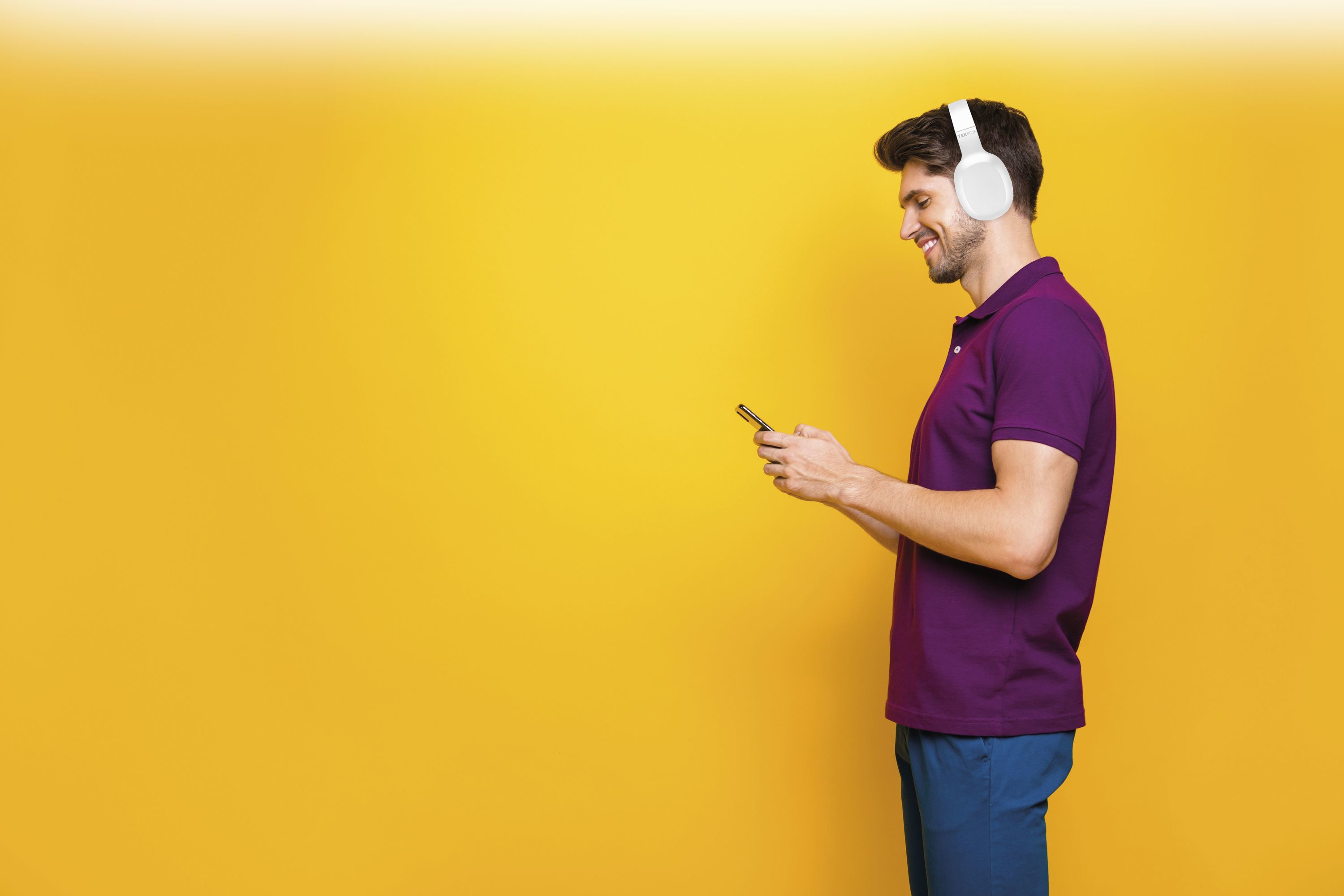 Mann mit Kopfhörern, lila Hemd und blauer Hose, der ein Telefon vor gelbem Hintergrund benutzt.