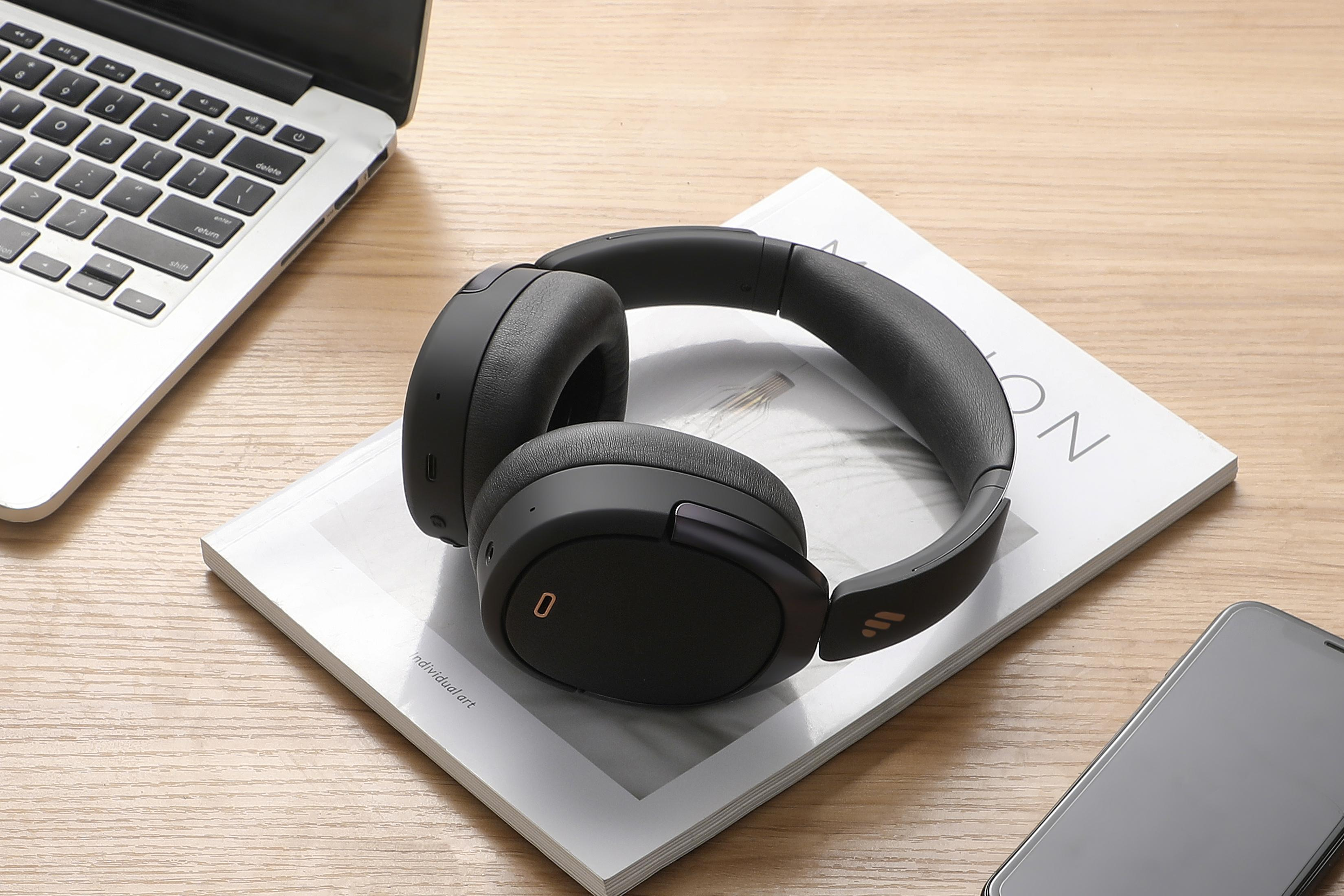 Para czarnych słuchawek na książce, laptop i smartfon na drewnianym stole.