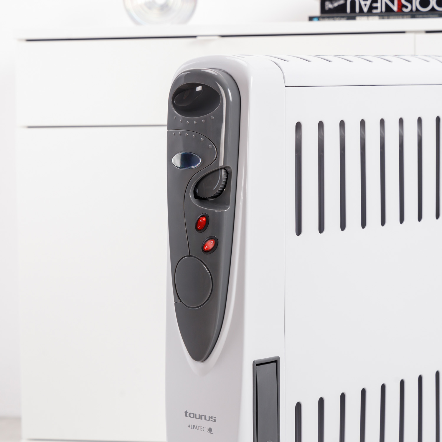 Un radiador de aceite Taurus Alpatec blanco y gris. Tiene un panel de control y ranuras verticales. El fondo es blanco.