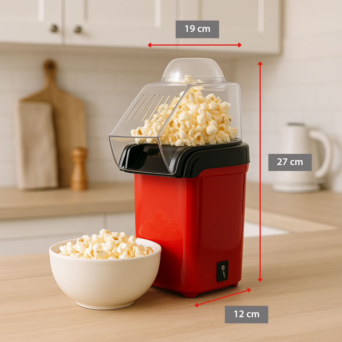 Red popcorn maker with popcorn inside and a bowl of popcorn next to it, on a wooden surface in a kitchen.
