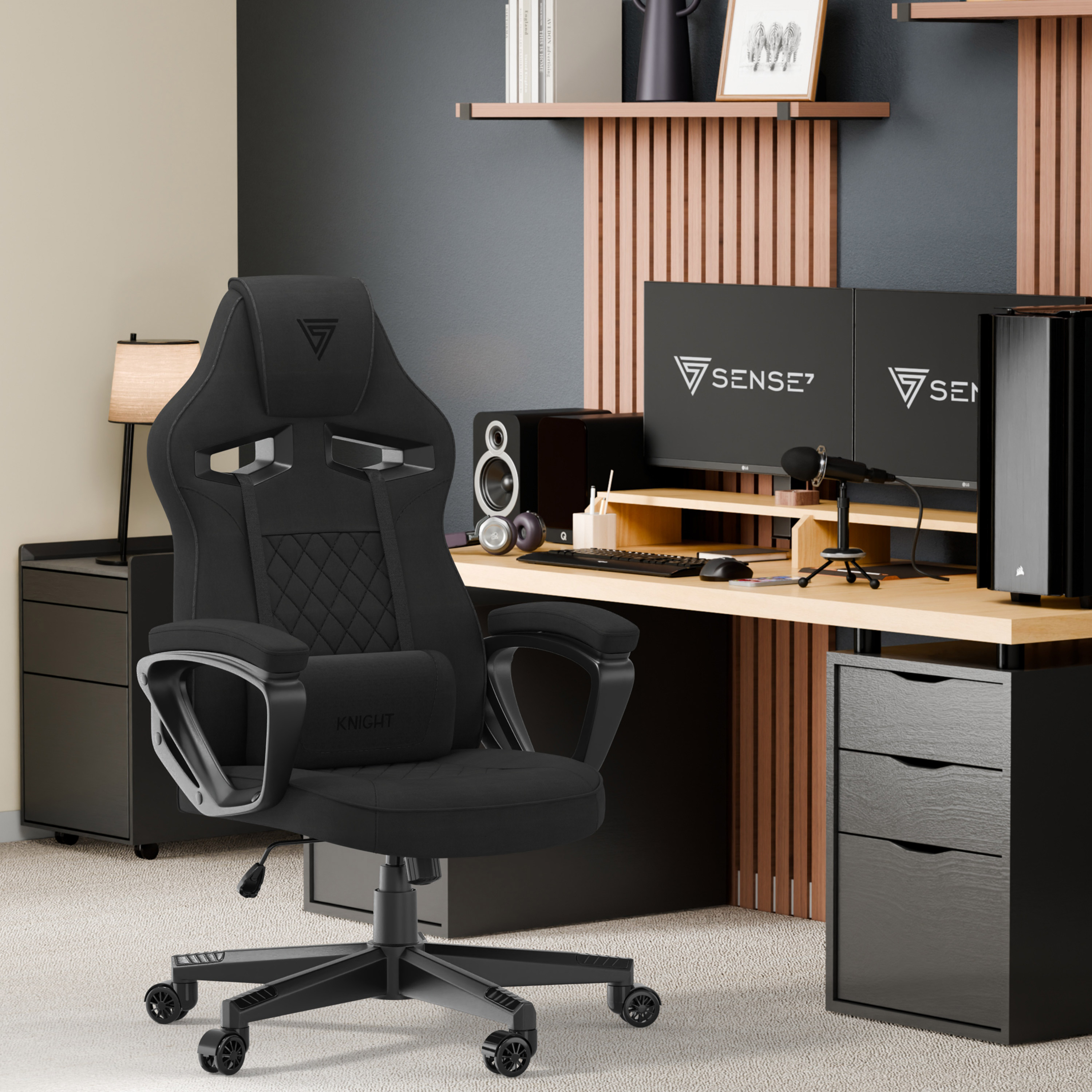 Zwarte gamestoel in een gamekamer. Twee monitoren, luidsprekers en een microfoon staan op het bureau.