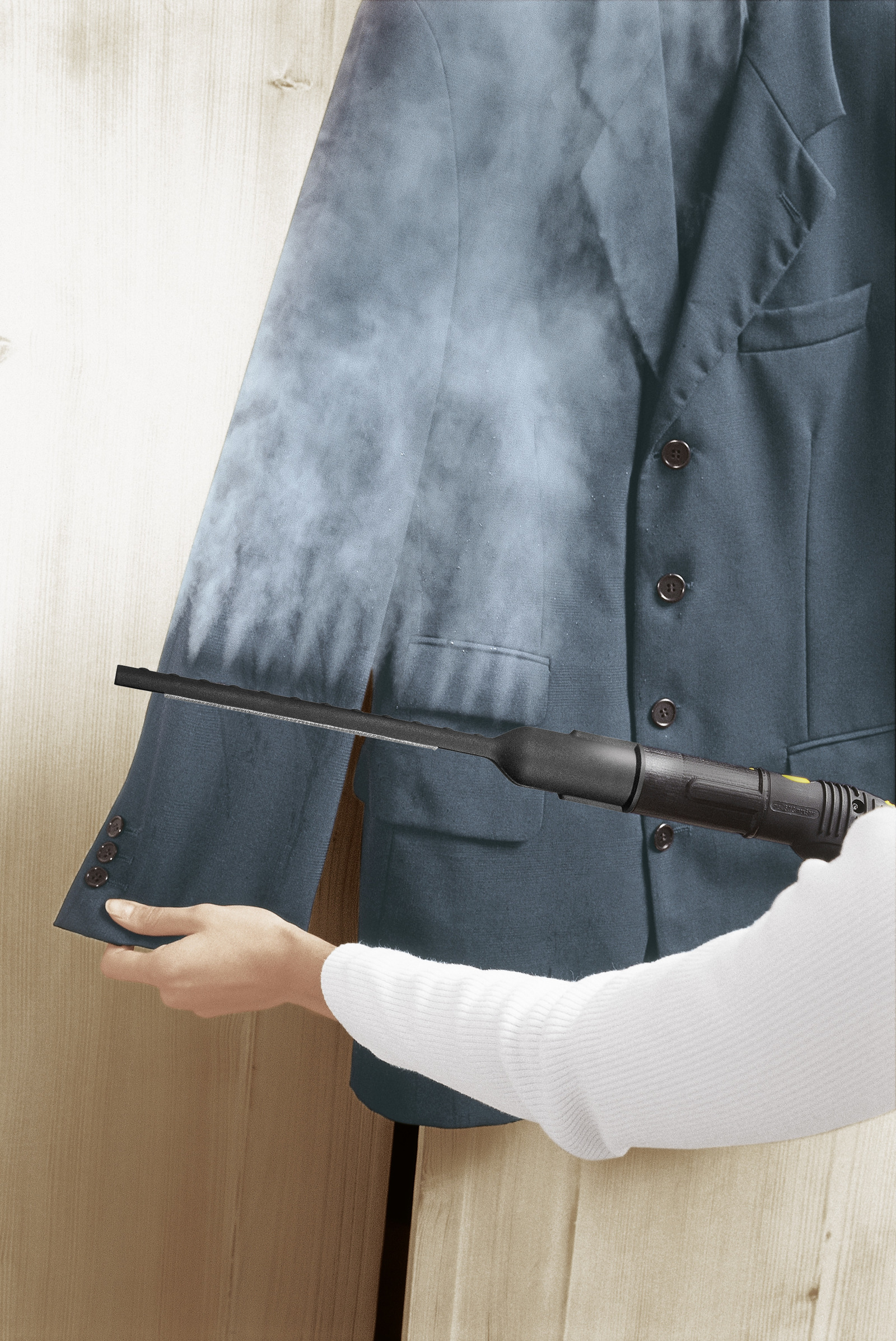 Una persona stira una giacca di un abito verde acqua con un vaporizzatore nero. Lo sfondo è una parete di legno.