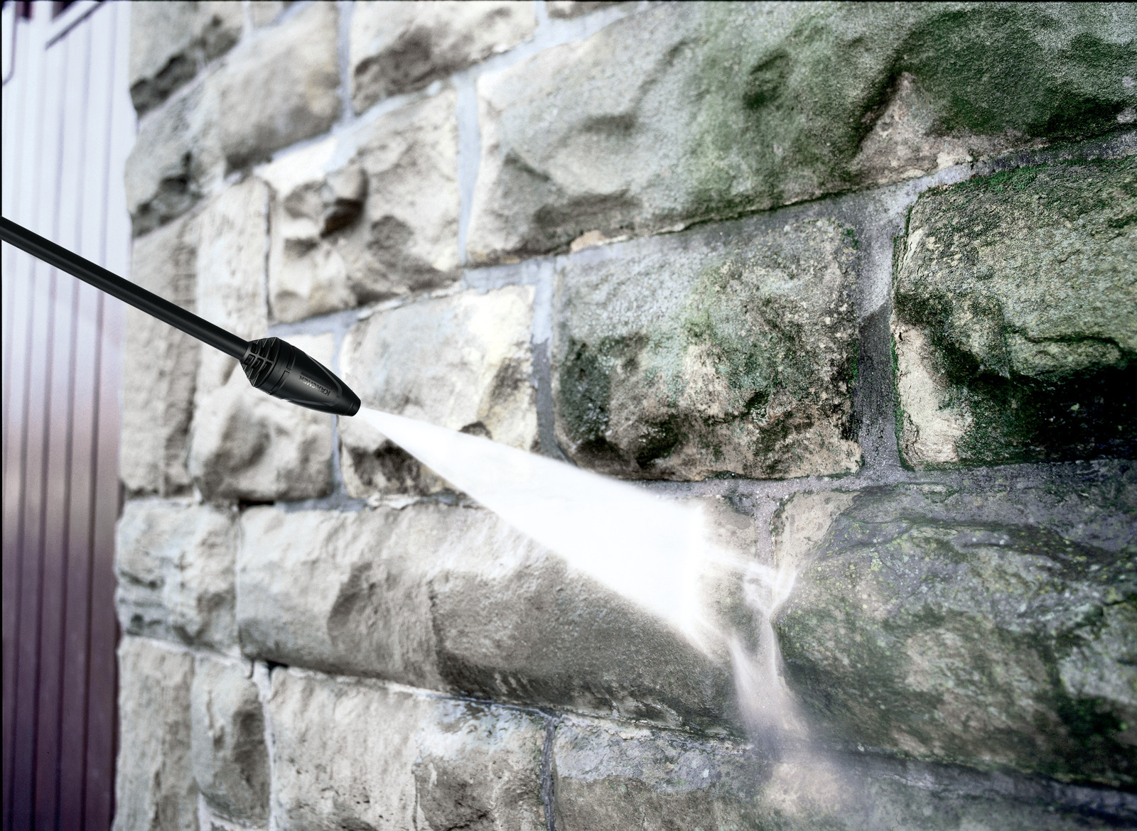 Un'idropulitrice spruzza un muro di pietra. Il muro è fatto di pietre grigie. L'acqua esce dall'ugello, pulendo il muro.