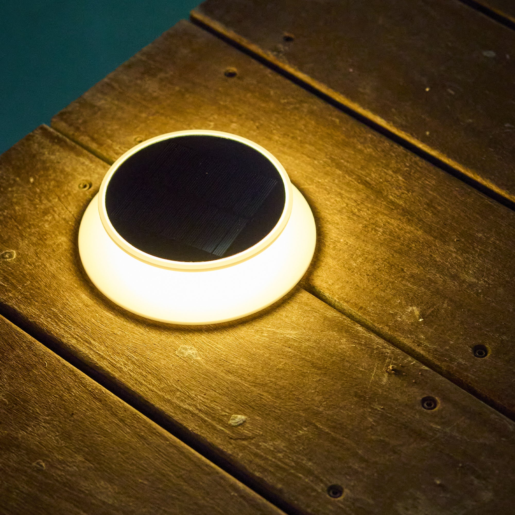Ein leuchtendes Solarlicht auf einer Holzoberfläche. Das Licht ist rund mit dunklem Zentrum. Das Holz ist braun.