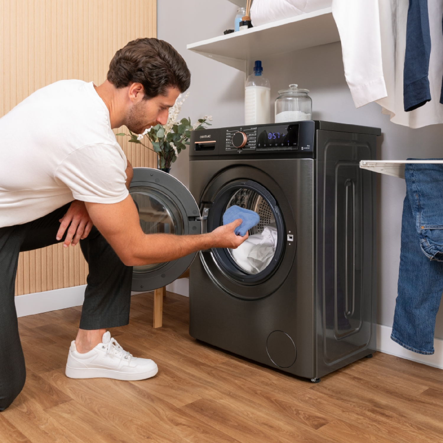 Un uomo carica una lavatrice. Indossa una camicia bianca e pantaloni neri. La macchina è grigia e c'è biancheria dentro.