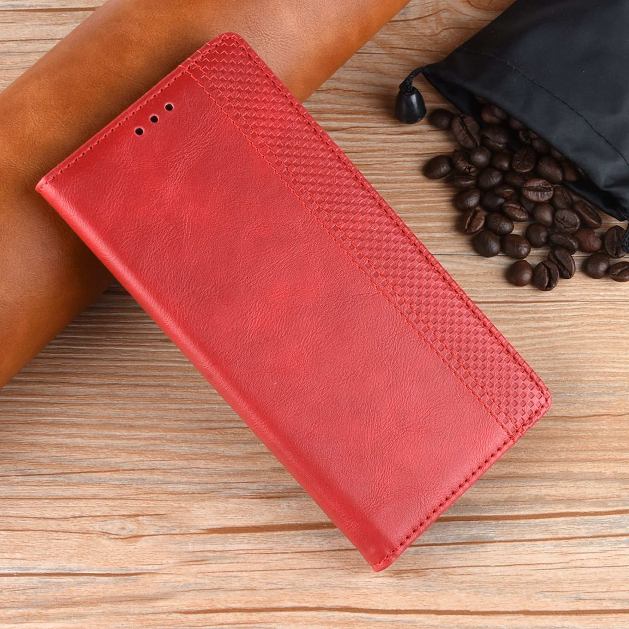 Eine rote Leder-Handyhülle auf Holz, mit Kaffeebohnen und einem schwarzen Beutel im Hintergrund.