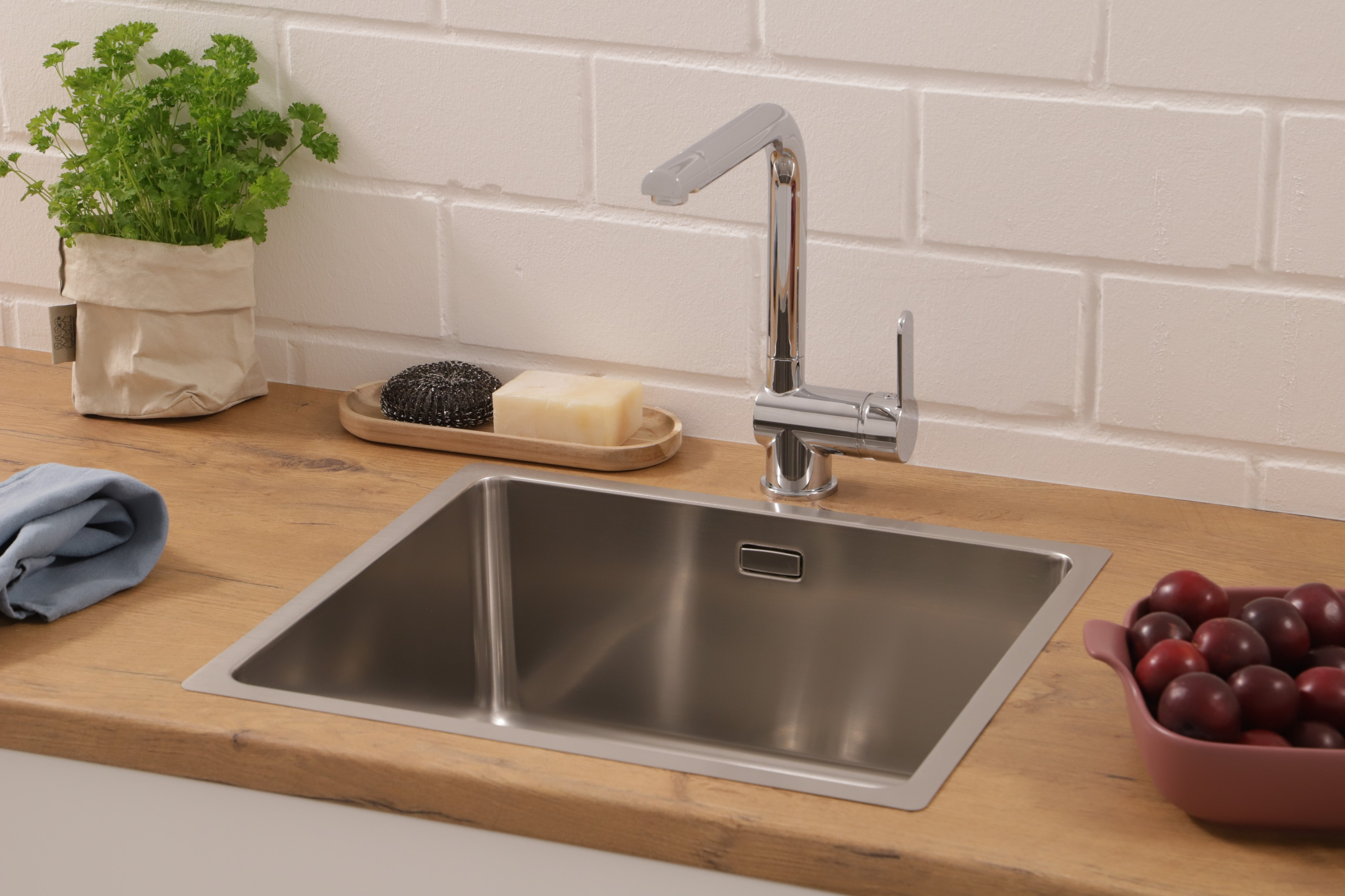 Ein Küchenwaschbecken mit Wasserhahn, Seife und einer Obstschale. Petersilie und ein blaues Tuch sind ebenfalls vorhanden.
