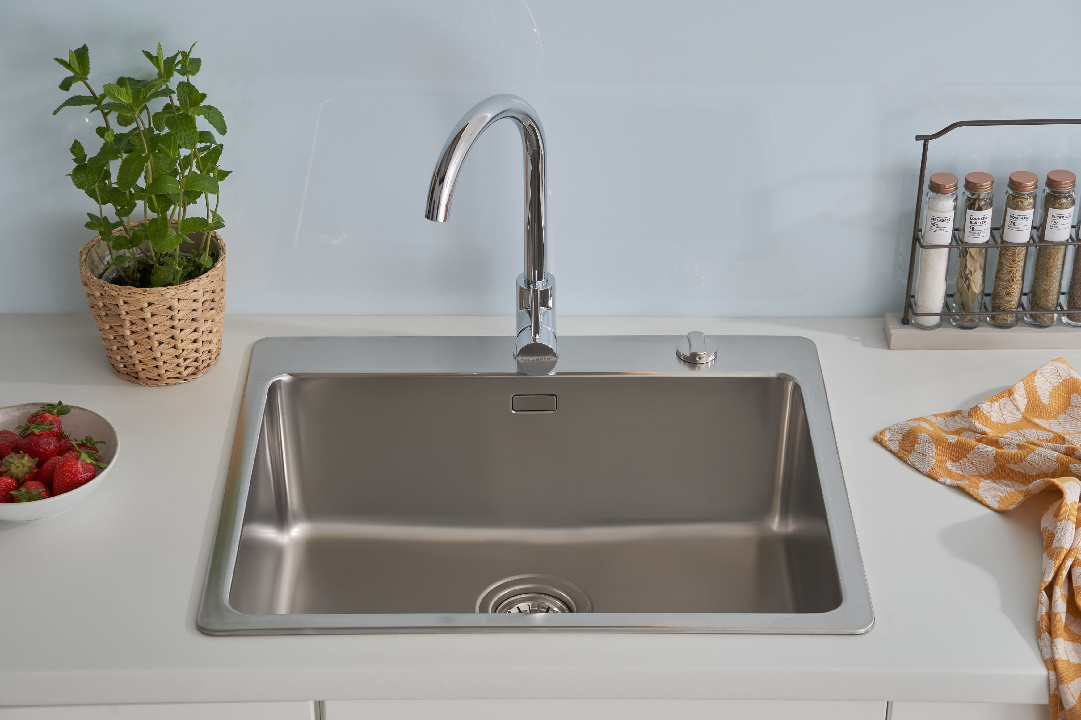 Edelstahl-Küchenspüle mit Wasserhahn, Erdbeeren, Minzepflanze und Gewürzen.