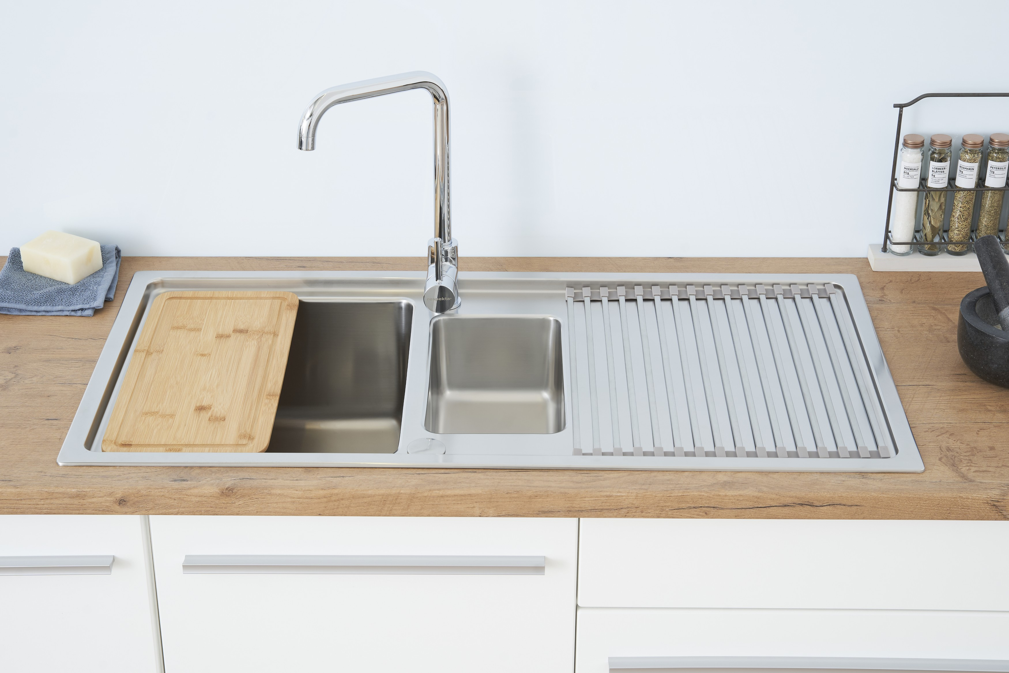 Ein Edelstahl-Küchenspülbecken mit einem Holzschneidebrett, einem Wasserhahn und Gewürzgläsern.