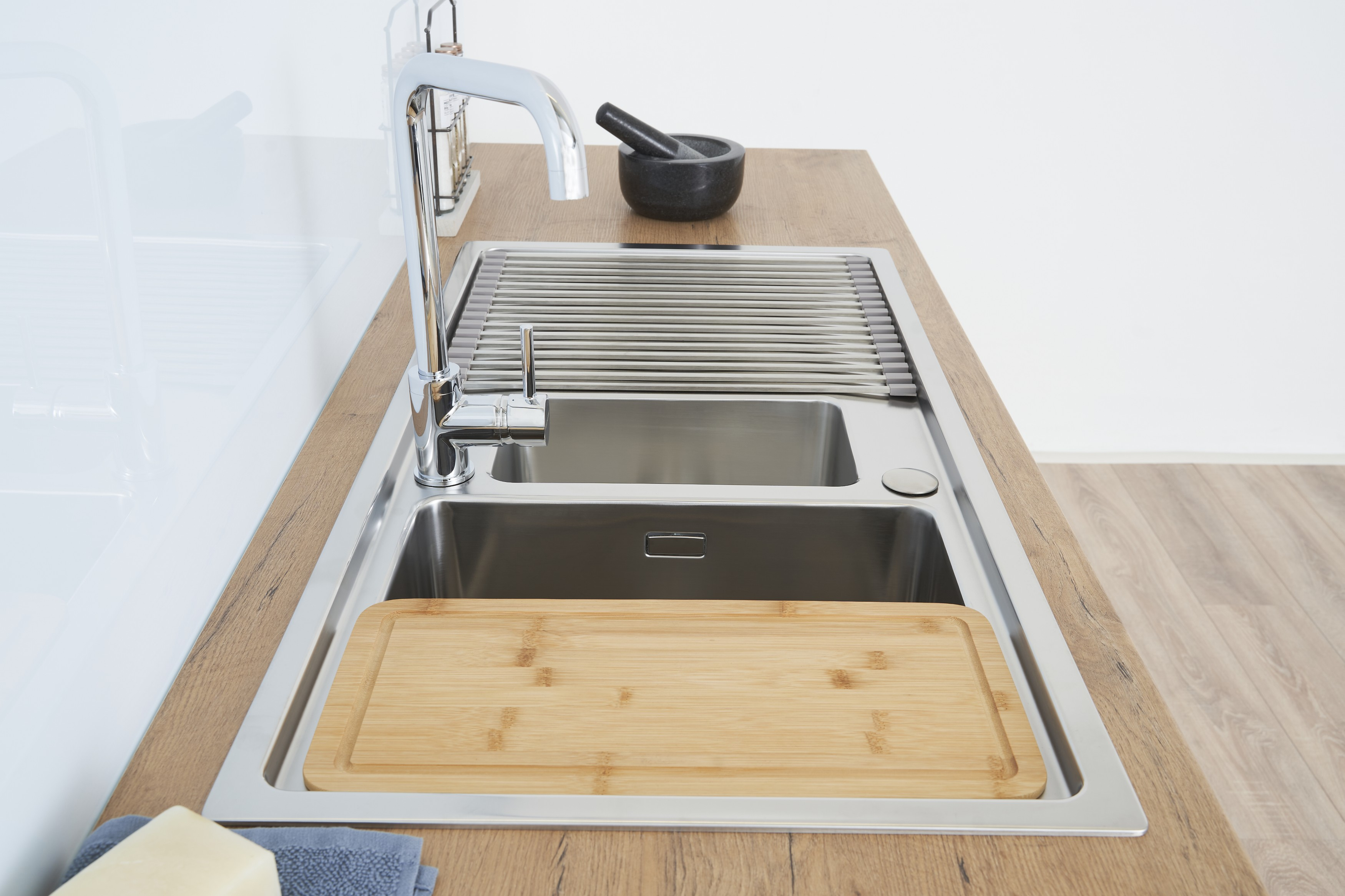Ein Edelstahl-Küchenbecken mit einem Holzschneidebrett, Wasserhahn und einem schwarzen Mörser auf einer Holzplatte.