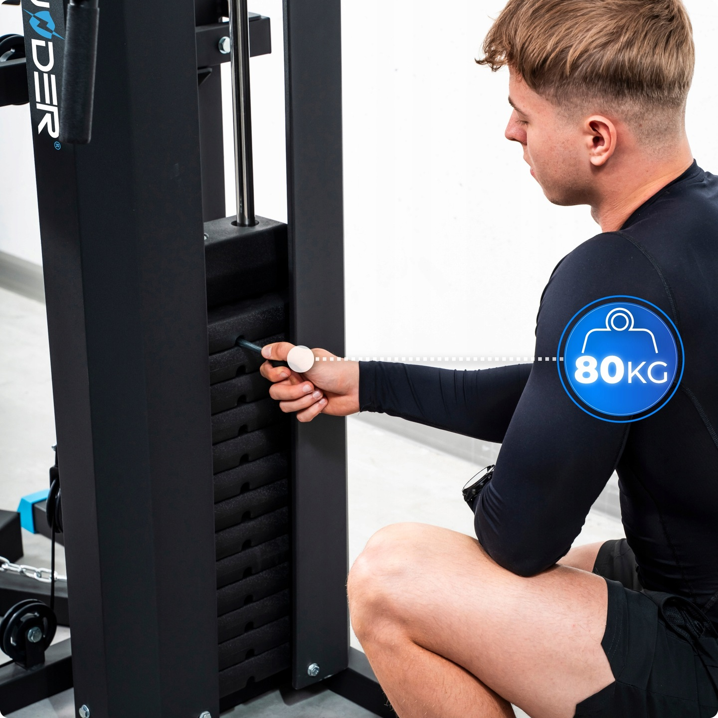 Mężczyzna w czarnym stroju sportowym reguluje maszynę do ćwiczeń. Widoczna ikona 80 KG. Maszyna jest czarna i ma metalowe części.
