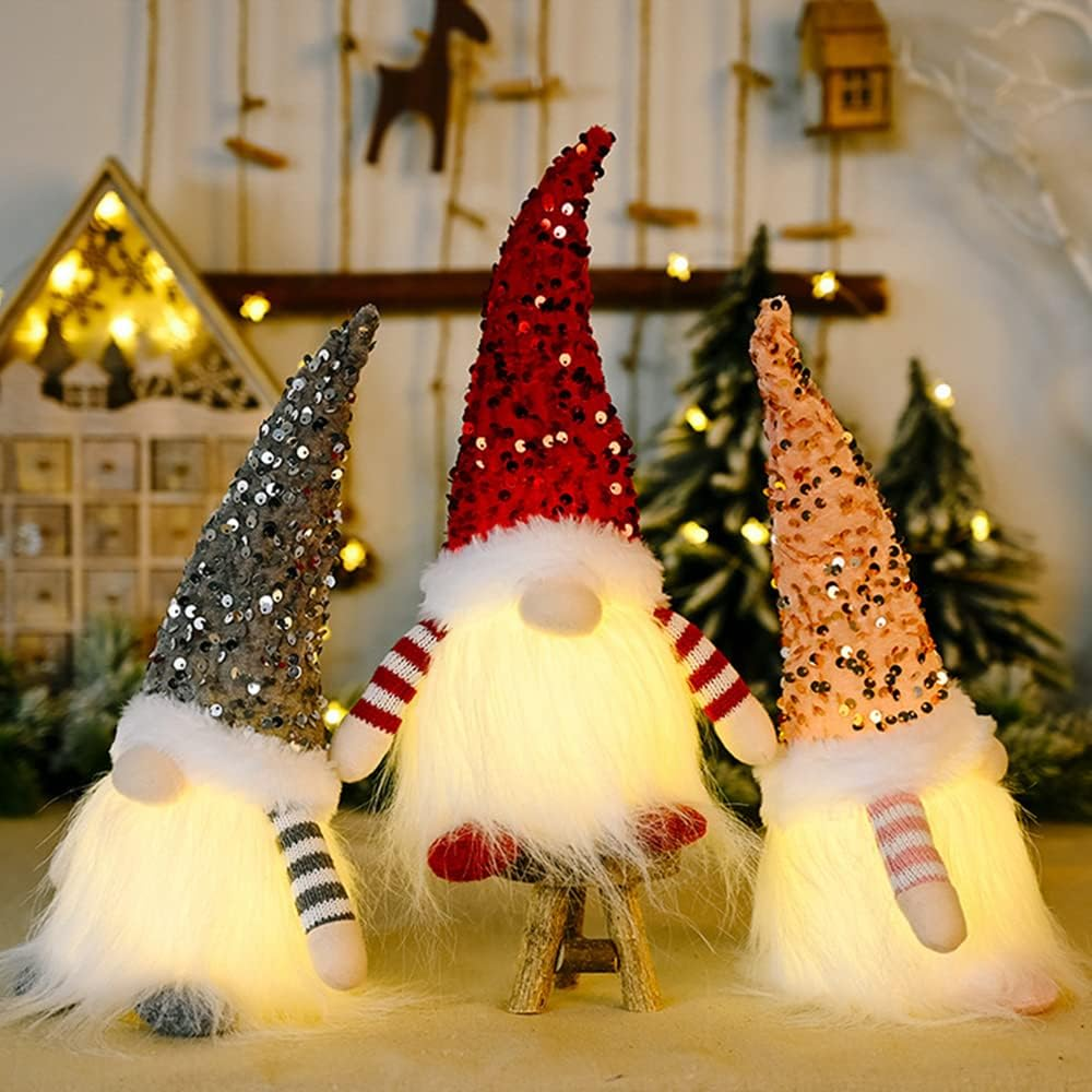 Drei beleuchtete Wichtel mit Paillettenhüten und flauschigen weißen Bärten. Der Hintergrund hat Weihnachtsbeleuchtung und Dekorationen.