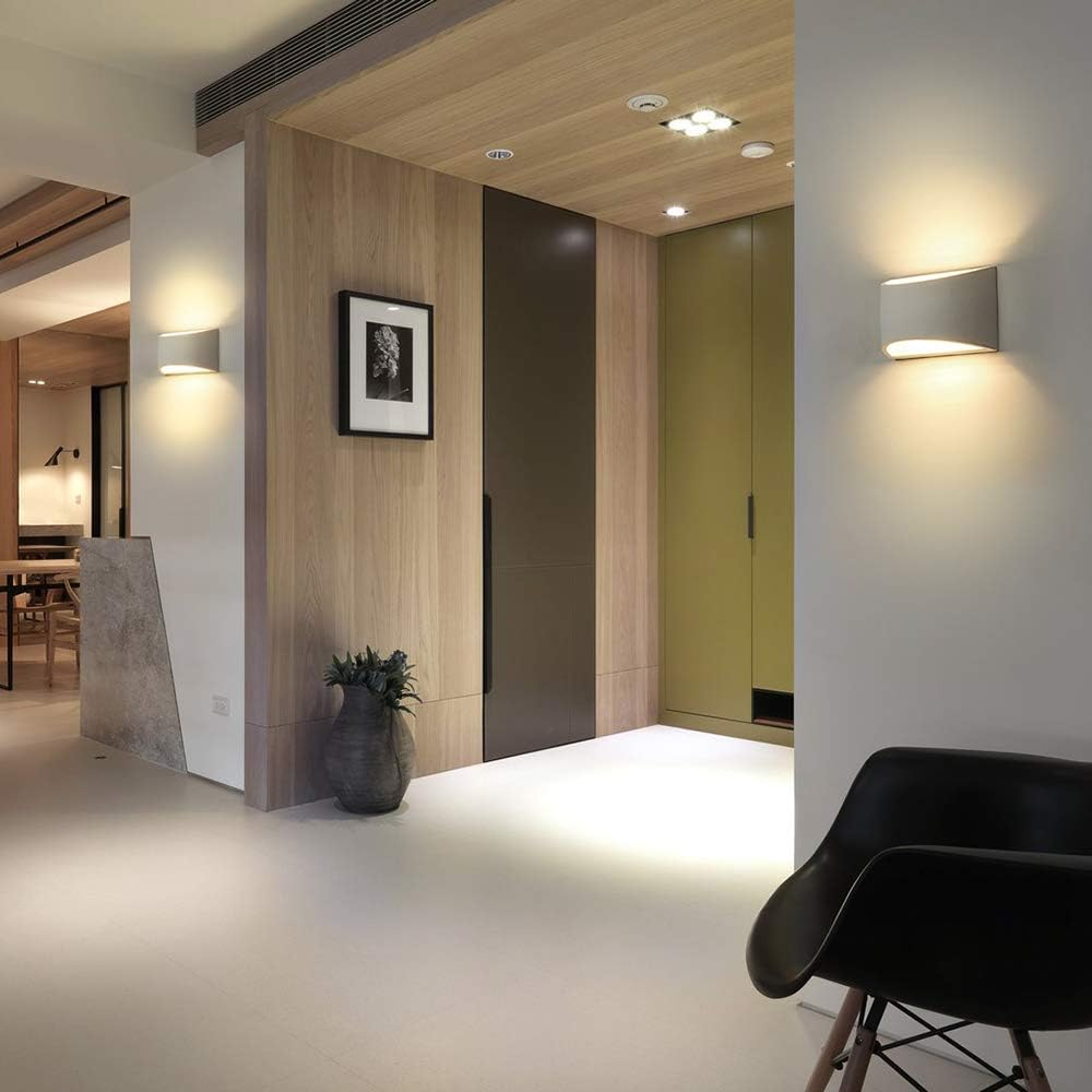 Ein modernes Interieur mit warmer Beleuchtung. Es gibt eine Vase, gerahmte Kunst und einen schwarzen Stuhl. Holzpaneele und weiße Wände.