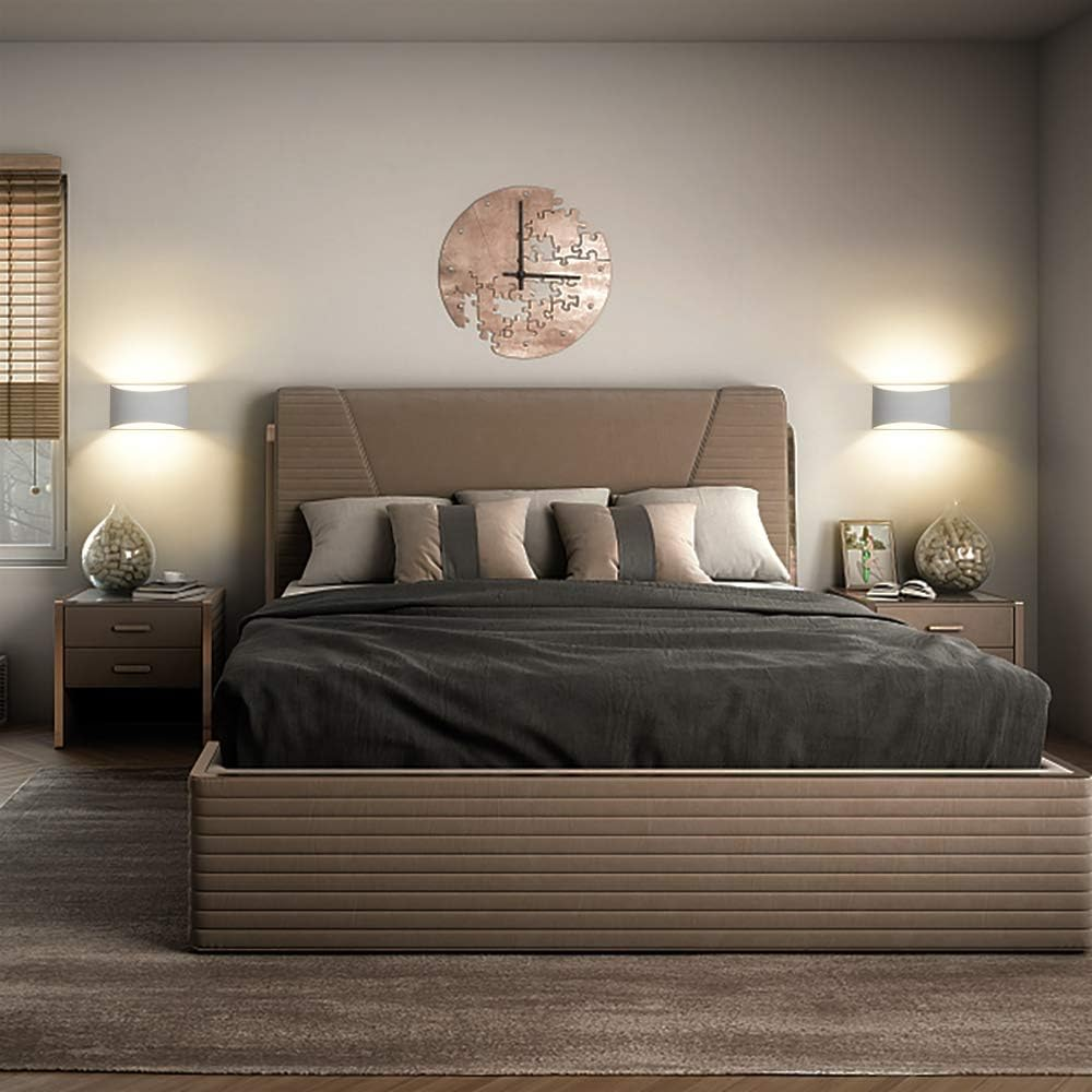 Schlafzimmer mit Bett, Kissen und Uhr. Zwei Lampen an den Wänden. Nachttische mit Lampen auf beiden Seiten des Bettes.