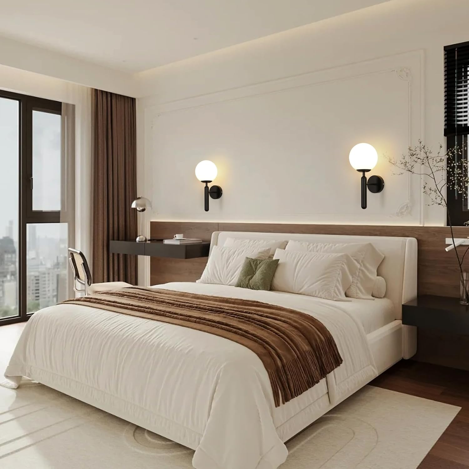 Ein Schlafzimmer mit Bett, Schreibtisch und großem Fenster. Das Bett hat weiße Bettwäsche und einen braunen Überwurf. Wandleuchten zieren die Wand.