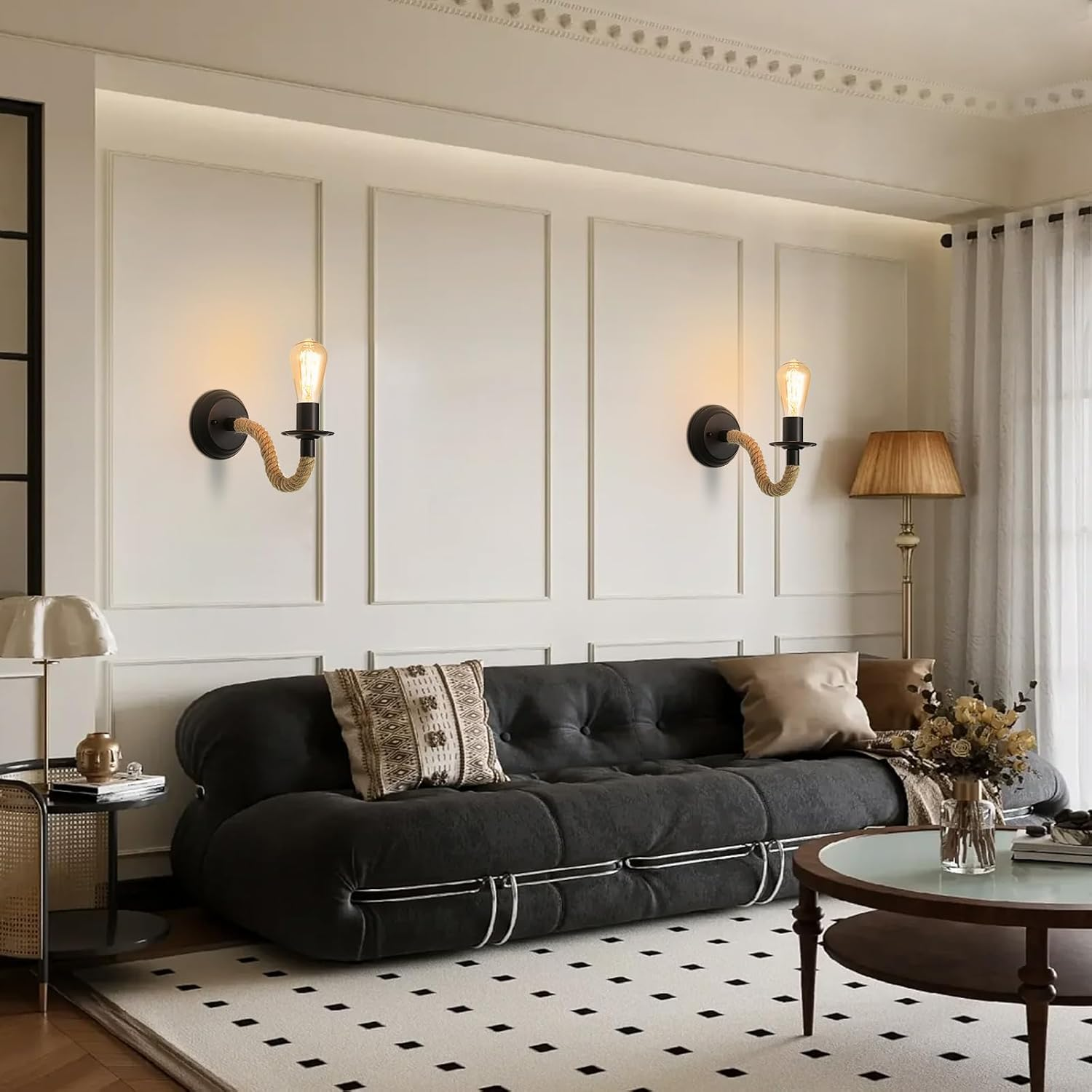 Ein Wohnzimmer mit schwarzem Sofa, zwei Wandlampen und einem Couchtisch. Die Wand ist weiß mit dekorativen Rahmen und einem gemusterten Teppich.