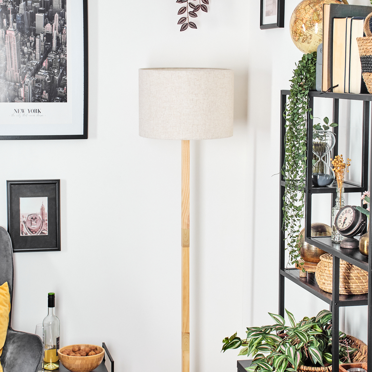 Ein Raum mit einer Lampe, Regalen und gerahmten Bildern. Ein Globus und Pflanzen sind ebenfalls zu sehen. Die Lampe steht im Mittelpunkt.