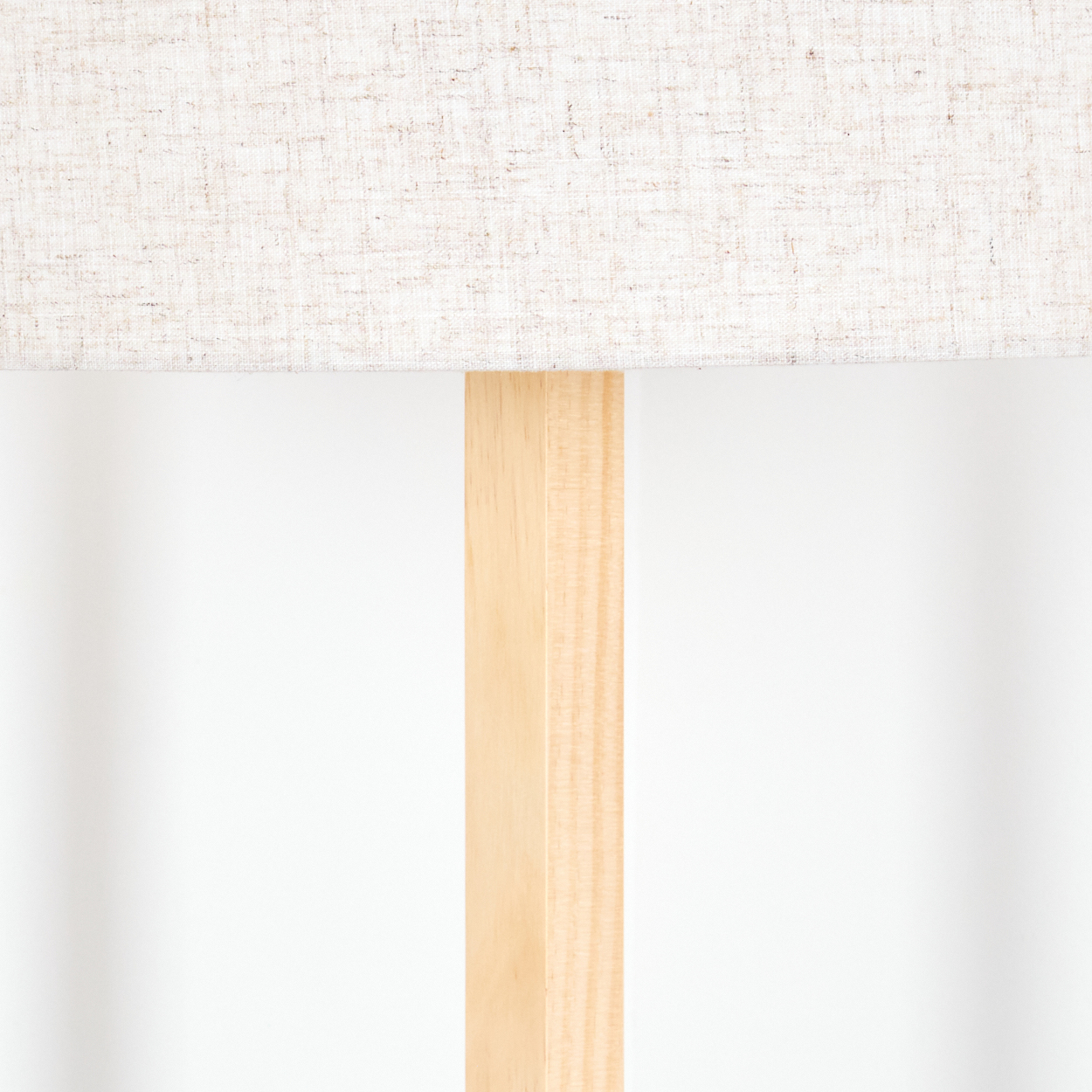 Ein beiger Lampenschirm sitzt auf einer hellen Holzlampe. Der Hintergrund ist eine schlichte, weiße Wand.