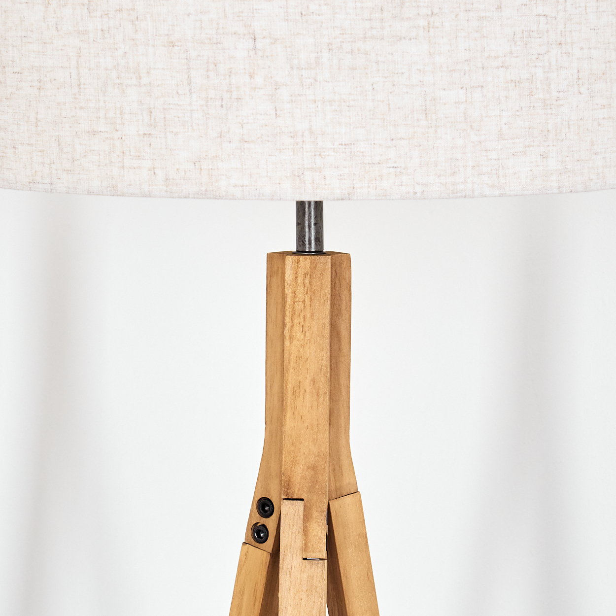 Eine hölzerne Stativlampe mit beigem Lampenschirm. Die Lampe steht auf weißem Hintergrund. Nahaufnahme.