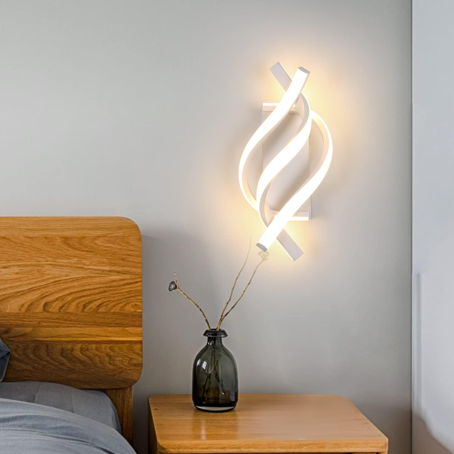 Ein modernes Schlafzimmer mit Wandlampe, Holzbett, Nachttisch und Vase mit Zweigen. Die Lampe hat ein Spiraldesign.
