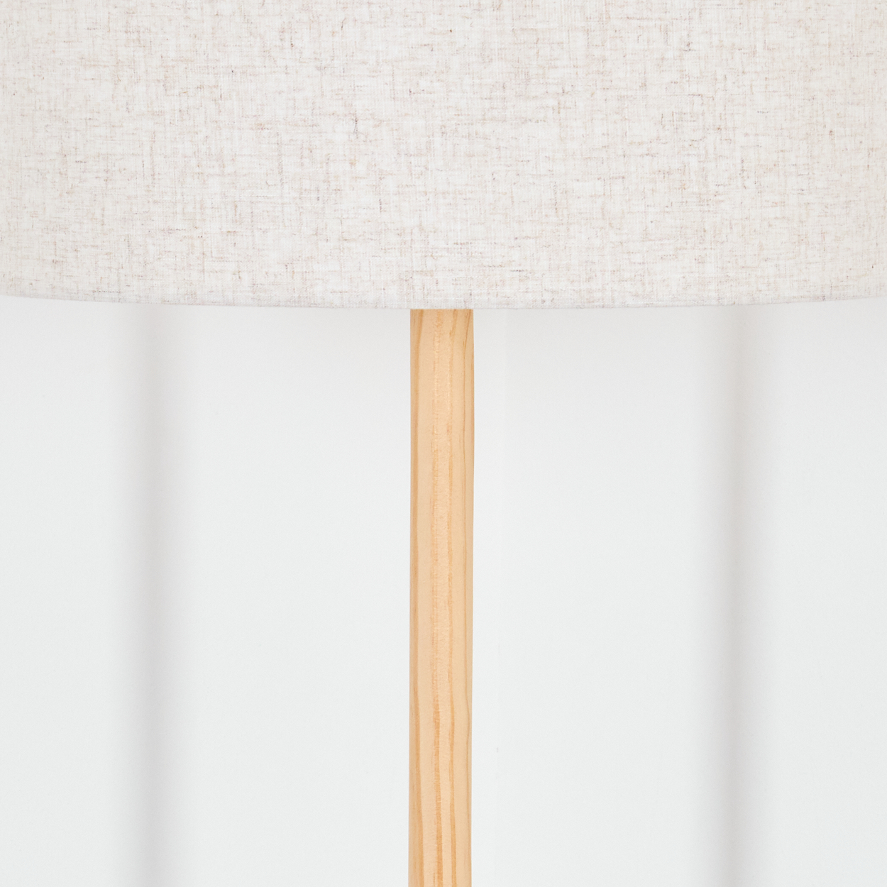 Ein beiger Lampenschirm sitzt auf einer Holzstange vor einer weißen Wand. Der Lampenschirm hat eine Stoffstruktur.