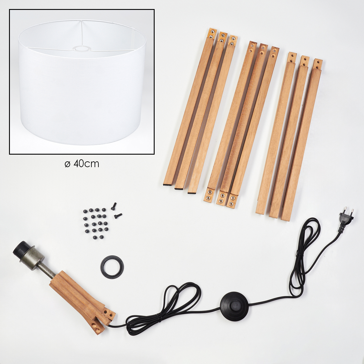 Eine zerlegte Lampe mit weißem Lampenschirm, Holzbeinen, Schrauben, Netzkabel und Lampenfassung auf weißem Untergrund.