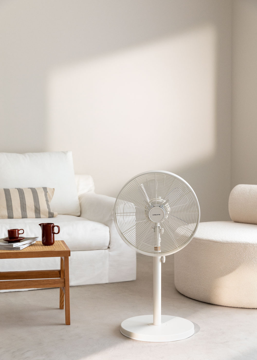 Un ventilador blanco en una habitación. Mesa con tazas, sofá y asiento redondeado. La habitación es luminosa.