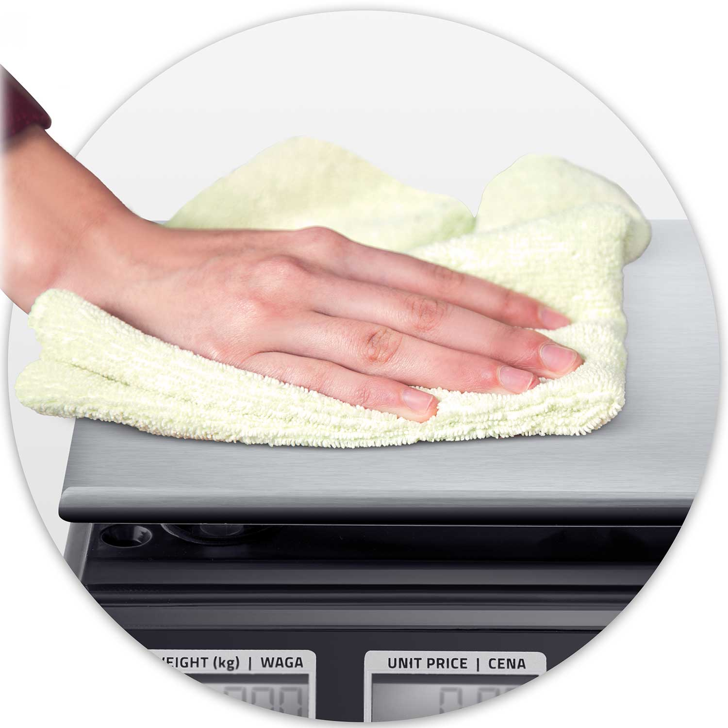 Ręka wyciera srebrną powierzchnię wagi jasnoniebieską szmatką. Waga ma czarną podstawę z cyfrowymi wyświetlaczami.