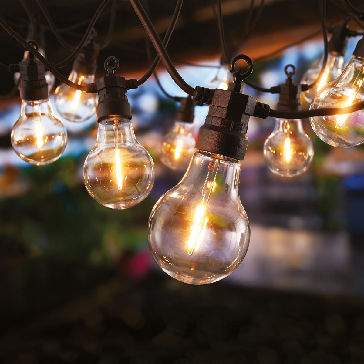 Close-up of string lights with glowing bulbs. Black wires and sockets. Out-of-focus background with hints of color.