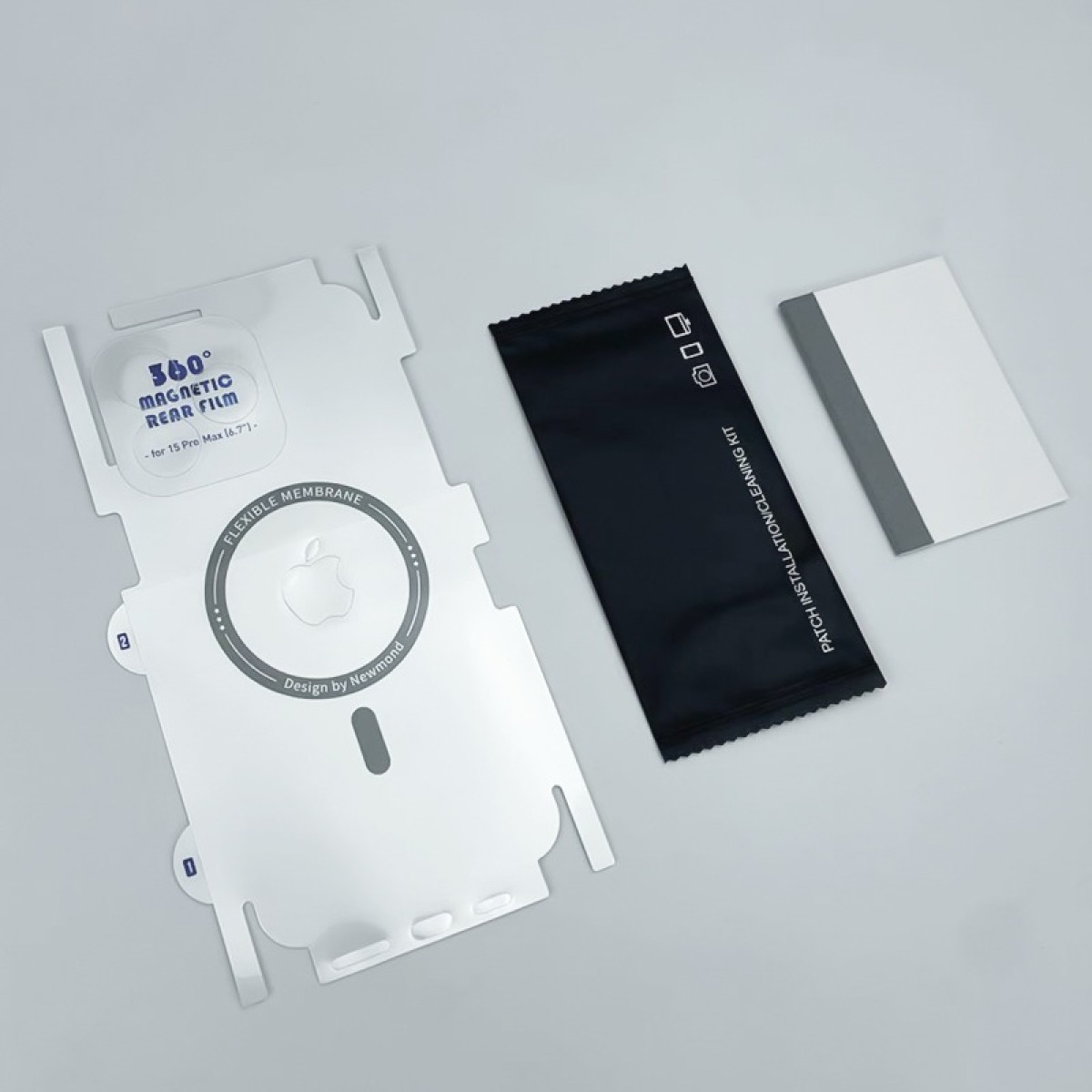 Kit per la protezione dello schermo del telefono: plastica bianca, panno per la pulizia nero e una carta bianca con striscia grigia, il tutto su una superficie grigia.