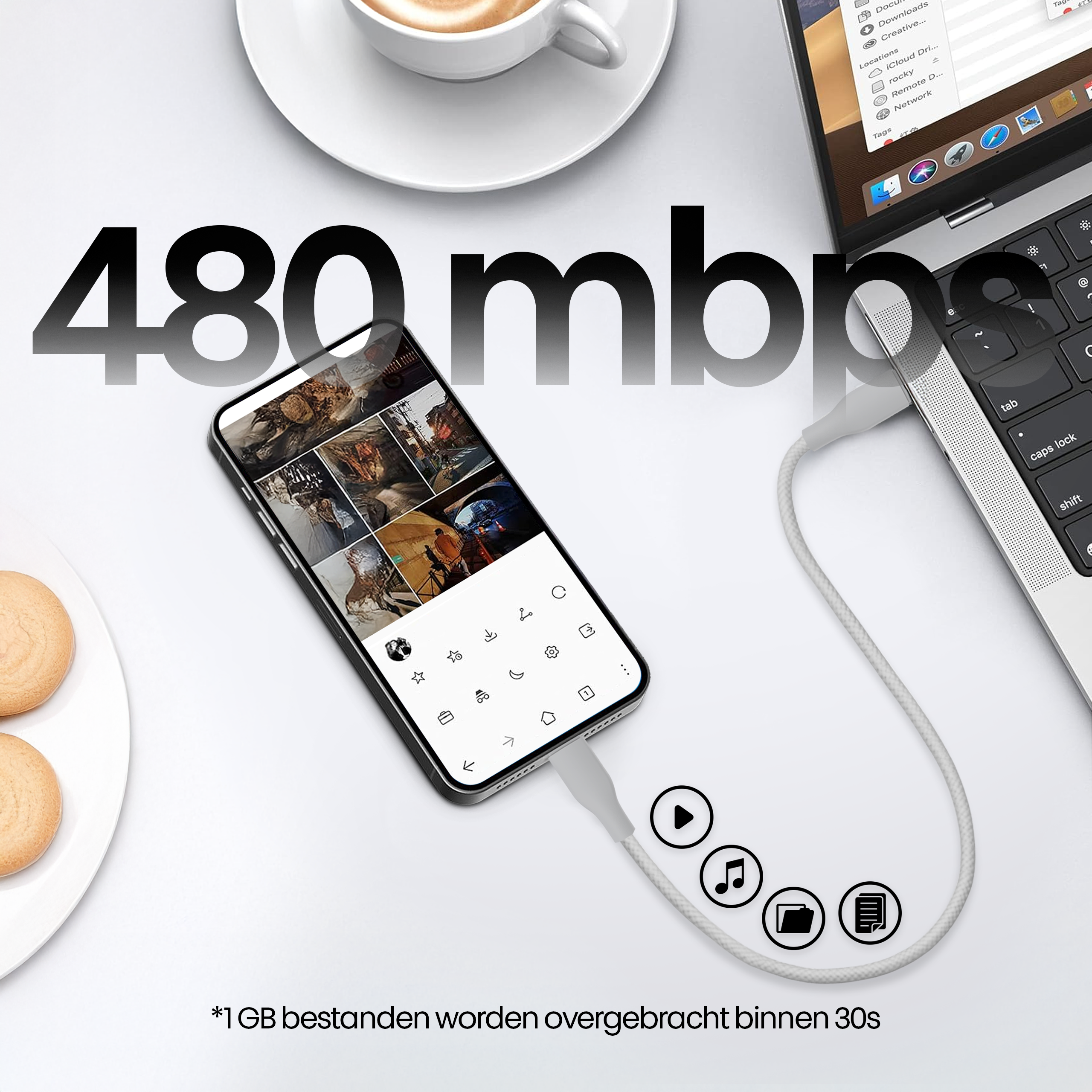 Een telefoon met foto's is via een kabel verbonden met een laptop. Een kopje koffie en gebakjes staan op tafel.