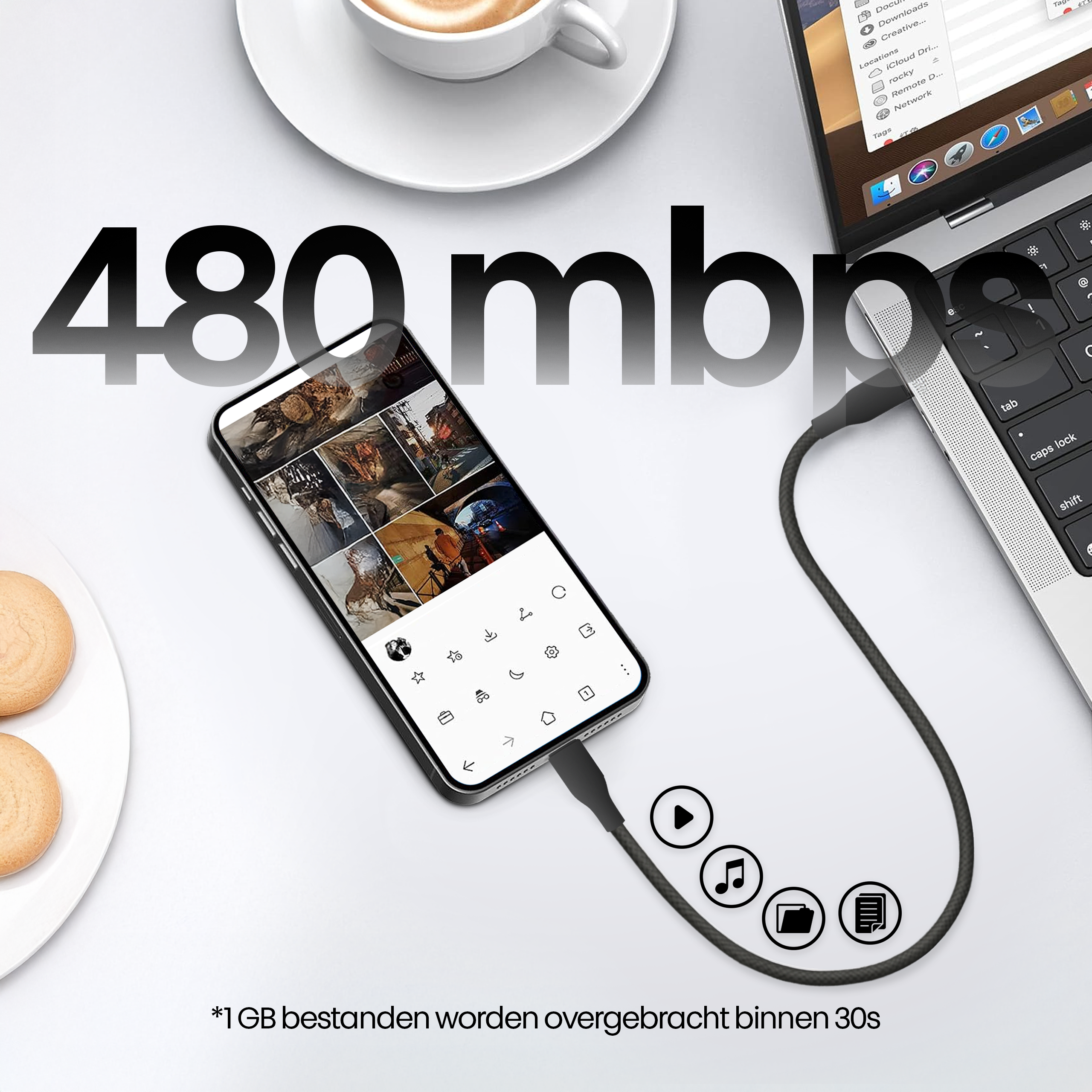Een telefoon verbonden met een laptop met een kabel. Een kopje koffie en koekjes op de achtergrond.