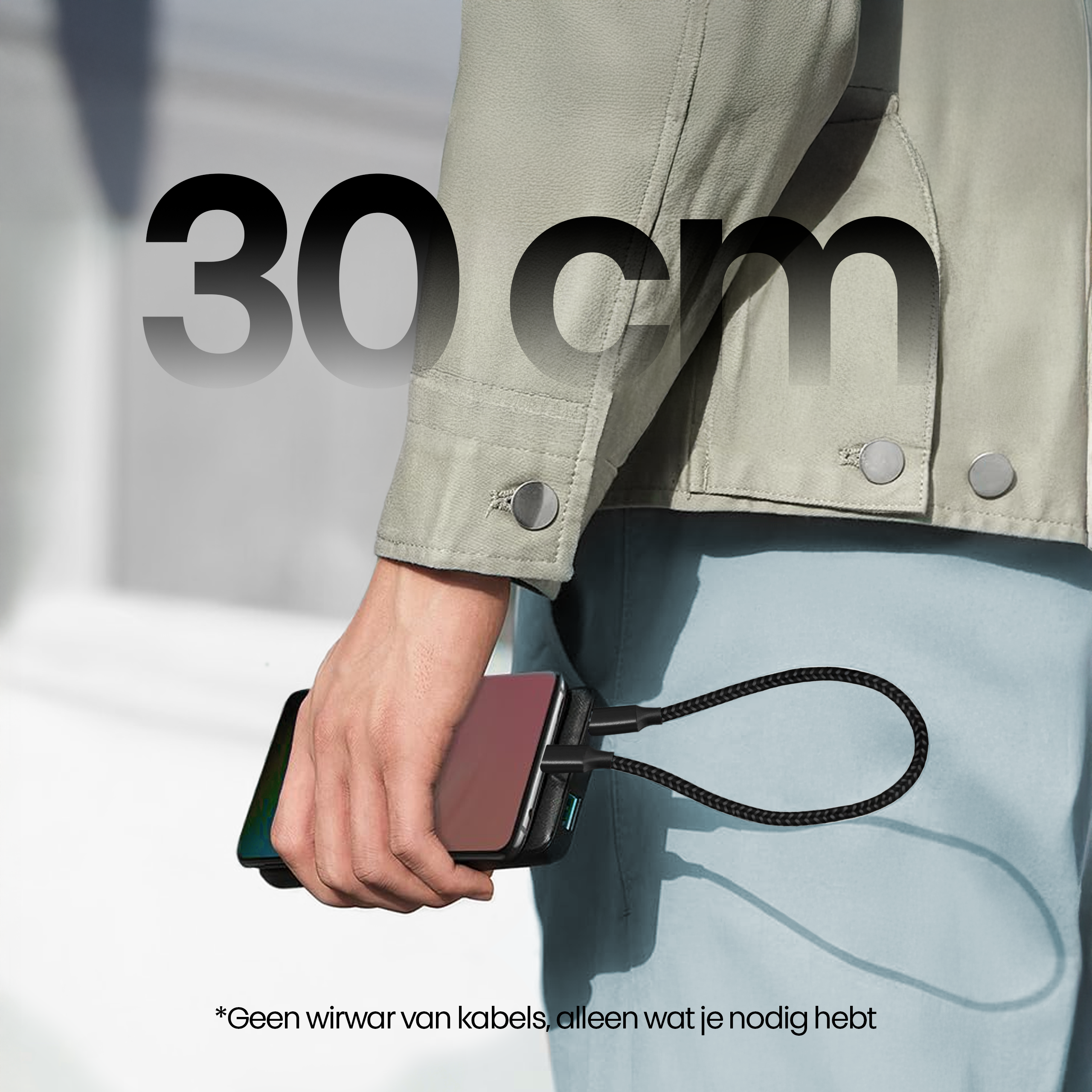 Een persoon houdt een telefoon vast die is aangesloten op een oplader. Tekst '30 cm' is zichtbaar. Jas en tekst in het Nederlands.