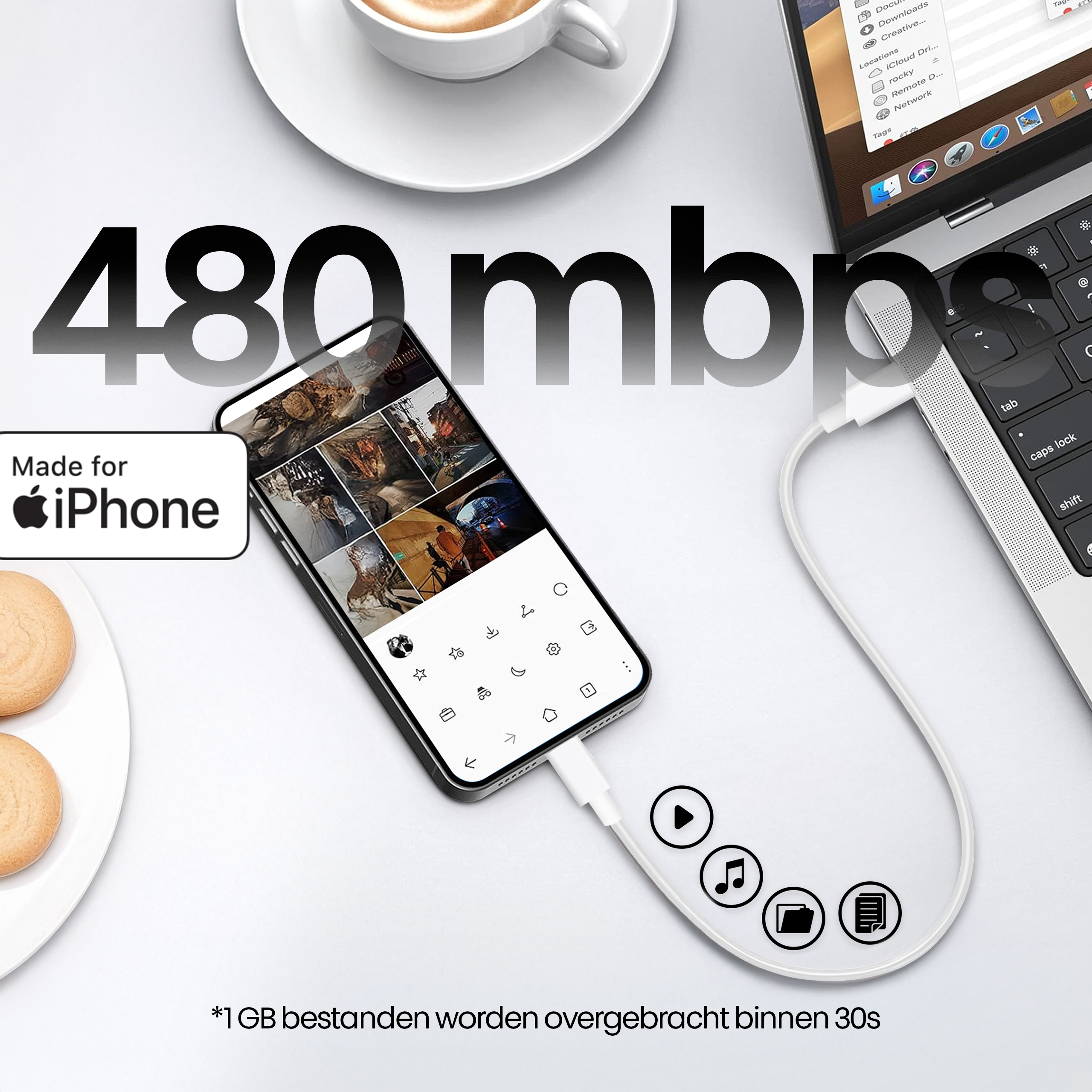 Een telefoon aangesloten op een laptop met een witte kabel. Een kopje koffie en koekjes zijn zichtbaar.