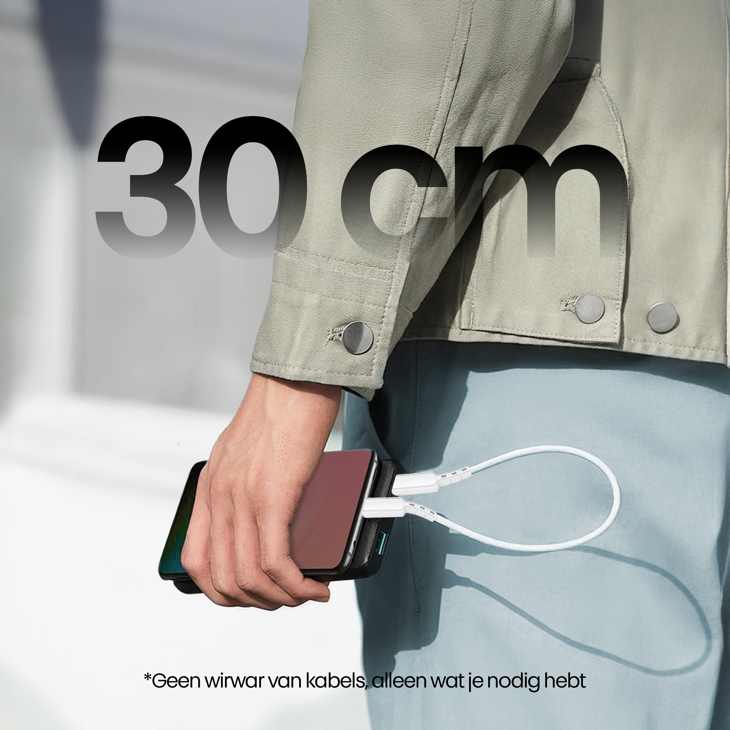 Een persoon houdt een telefoon vast die oplaadt met een witte kabel, met 30 cm tekst. De persoon draagt een jas.