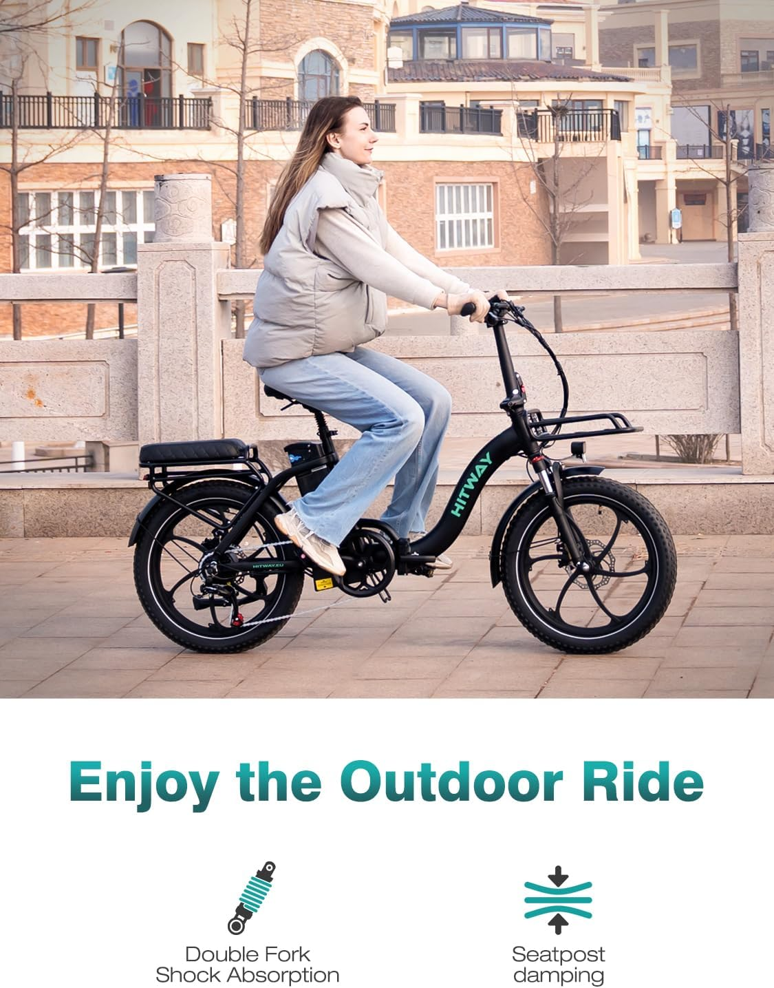 A woman rides a black HITWAY e-bike. She wears a vest and jeans. The background shows buildings and a stone bridge.