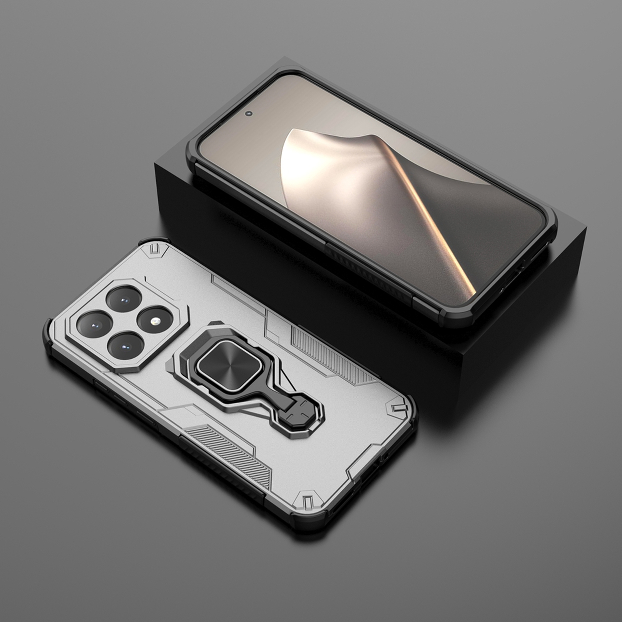 Twee zilverkleurige telefoonhoesjes met zwarte randen en ringhouders op een donkere ondergrond. Eén hoesje ligt op een zwart blok.