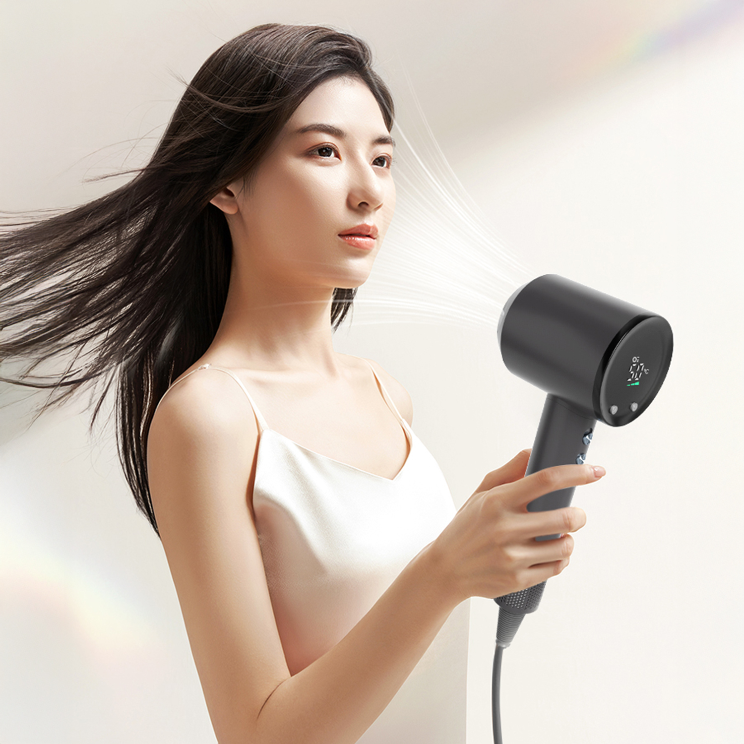 Una donna tiene un asciugacapelli nero, i capelli che soffiano indietro. Lo sfondo è chiaro con effetto arcobaleno.