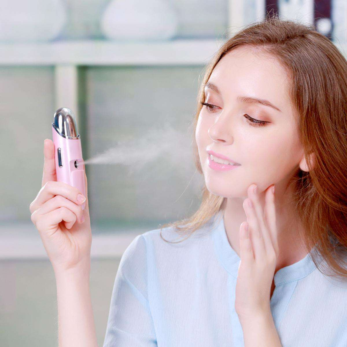 Eine Frau hält ein rosa Gesichtsspray-Gerät und sprüht es auf ihr Gesicht. Sie berührt ihre Wange mit der anderen Hand.