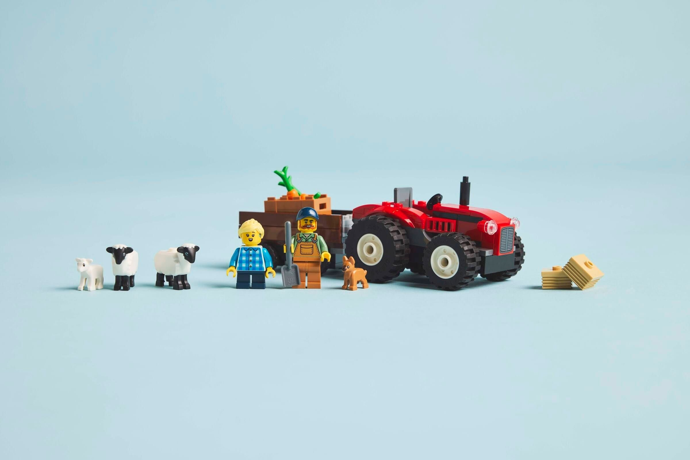 Eine Lego-Bauernhofszene mit Figuren, Traktor, Schafen und einem Hund auf hellblauem Hintergrund.
