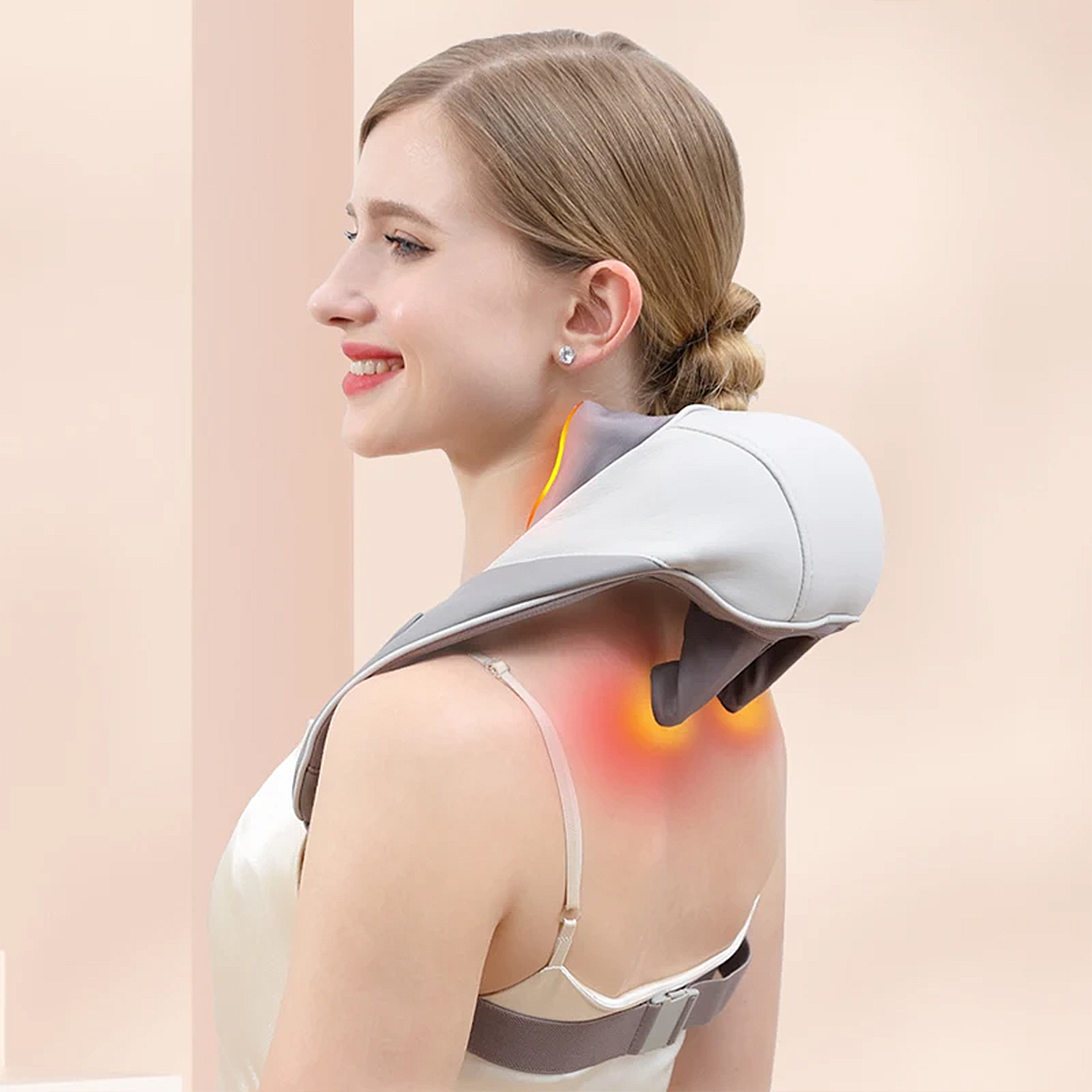 Mujer con un masajeador de cuello. Ella sonríe. El masajeador es gris y blanco. El fondo es rosa claro.