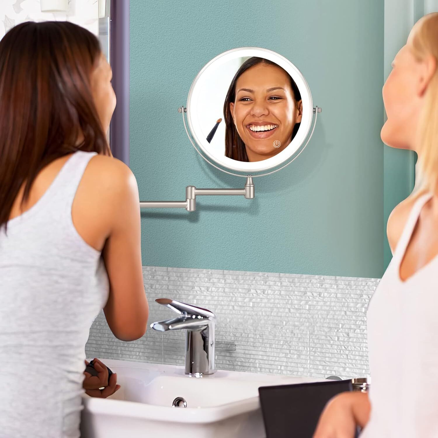 Zwei Frauen an einem Spiegel. Eine schminkt sich. Spiegelbild einer lächelnden Frau. Badezimmer mit Waschbecken und blauer Wand.